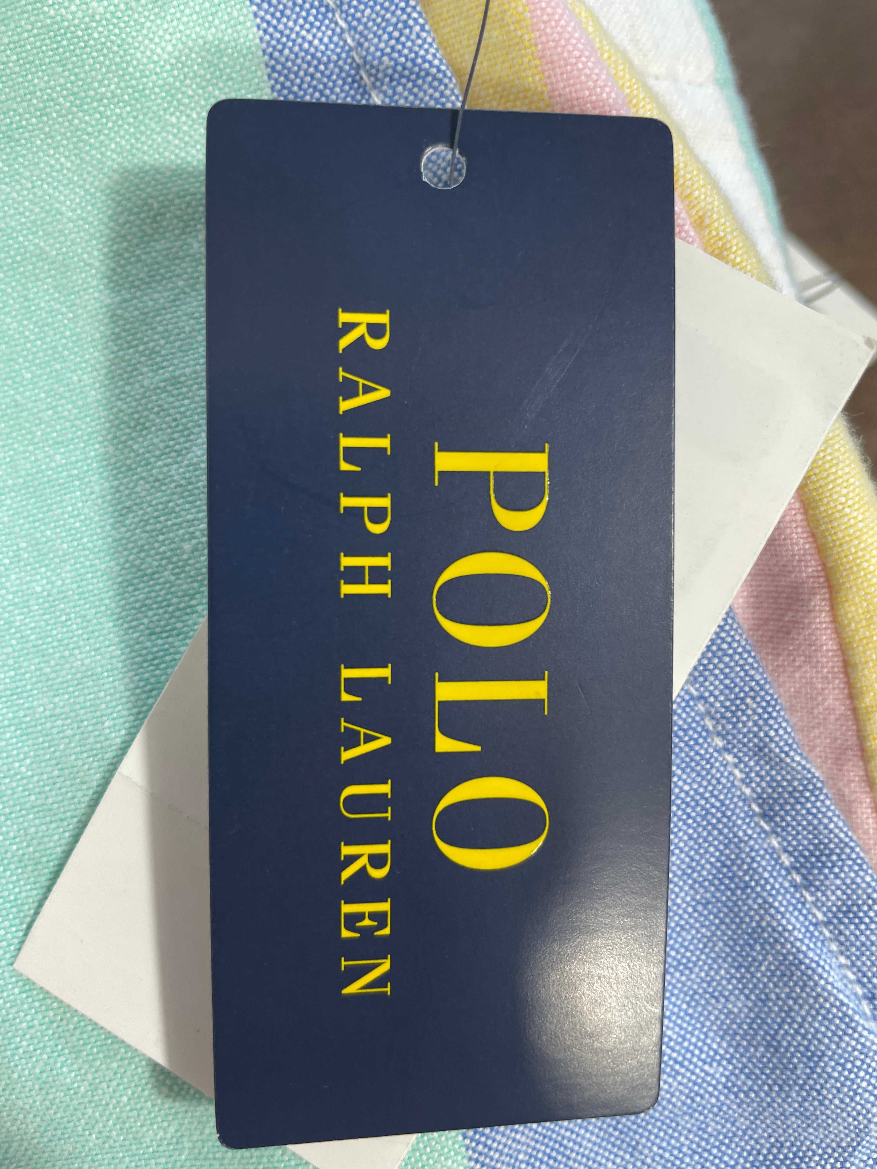 A navy blue Ralph Lauren Polo tag with yellow lettering, attached to a striped pastel garment.