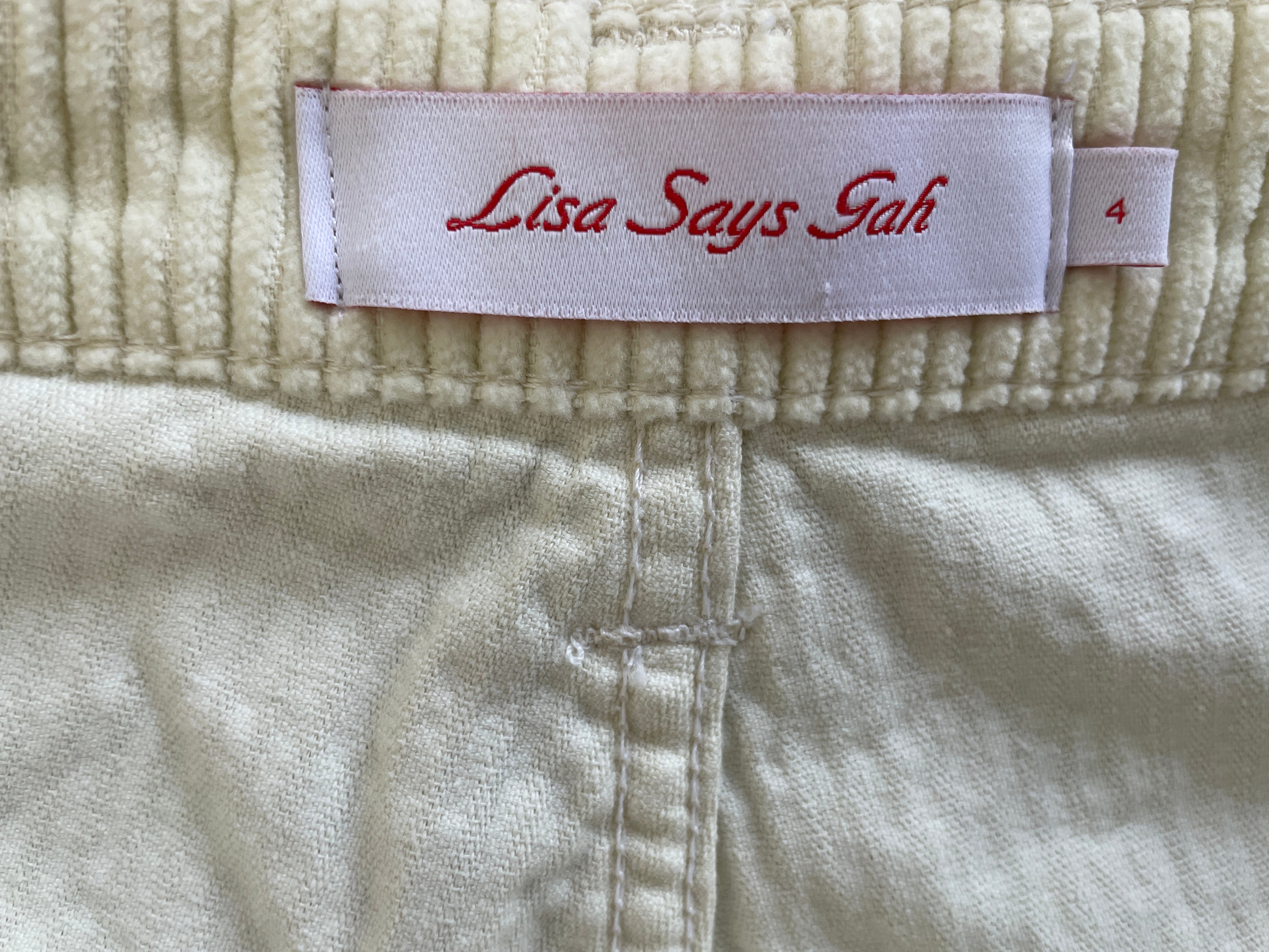 Close-up of a cream-colored ribbed knit garment with a sewn-in label reading 'Lisa Says Tah' in red script, with a small size tag showing '4'.