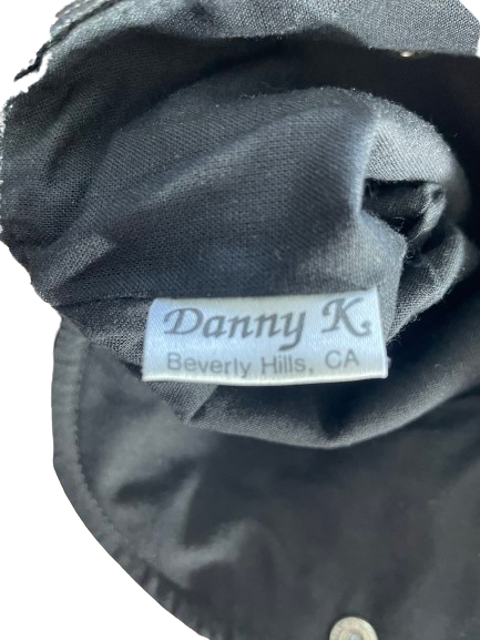 Close-up of a black fabric garment showing a sewn-on brand label that reads 'Danny K Beverly Hills, CA'.
