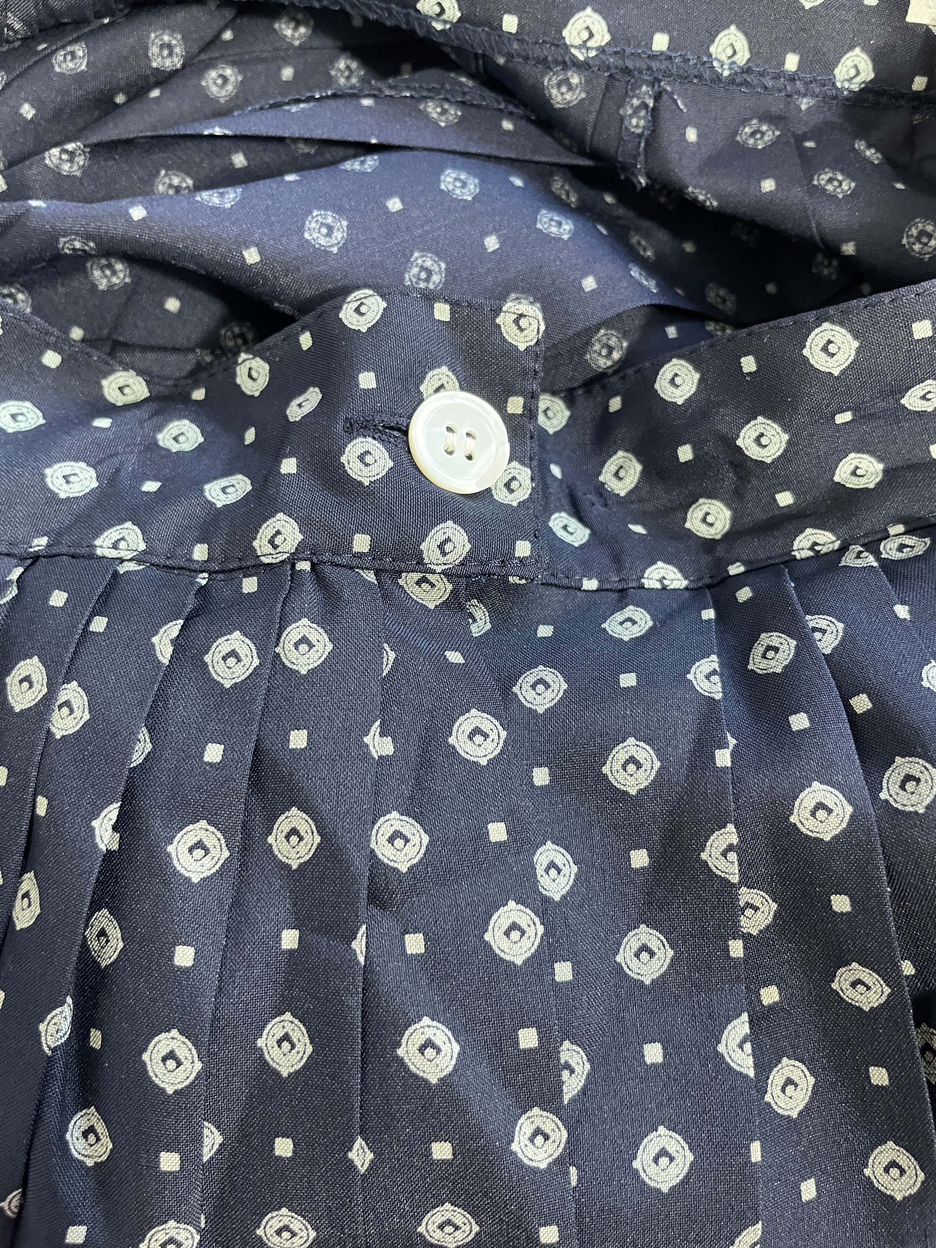 Close-up of a navy blue pleated fabric garment with a repeating white geometric pattern and a white button at the collar.