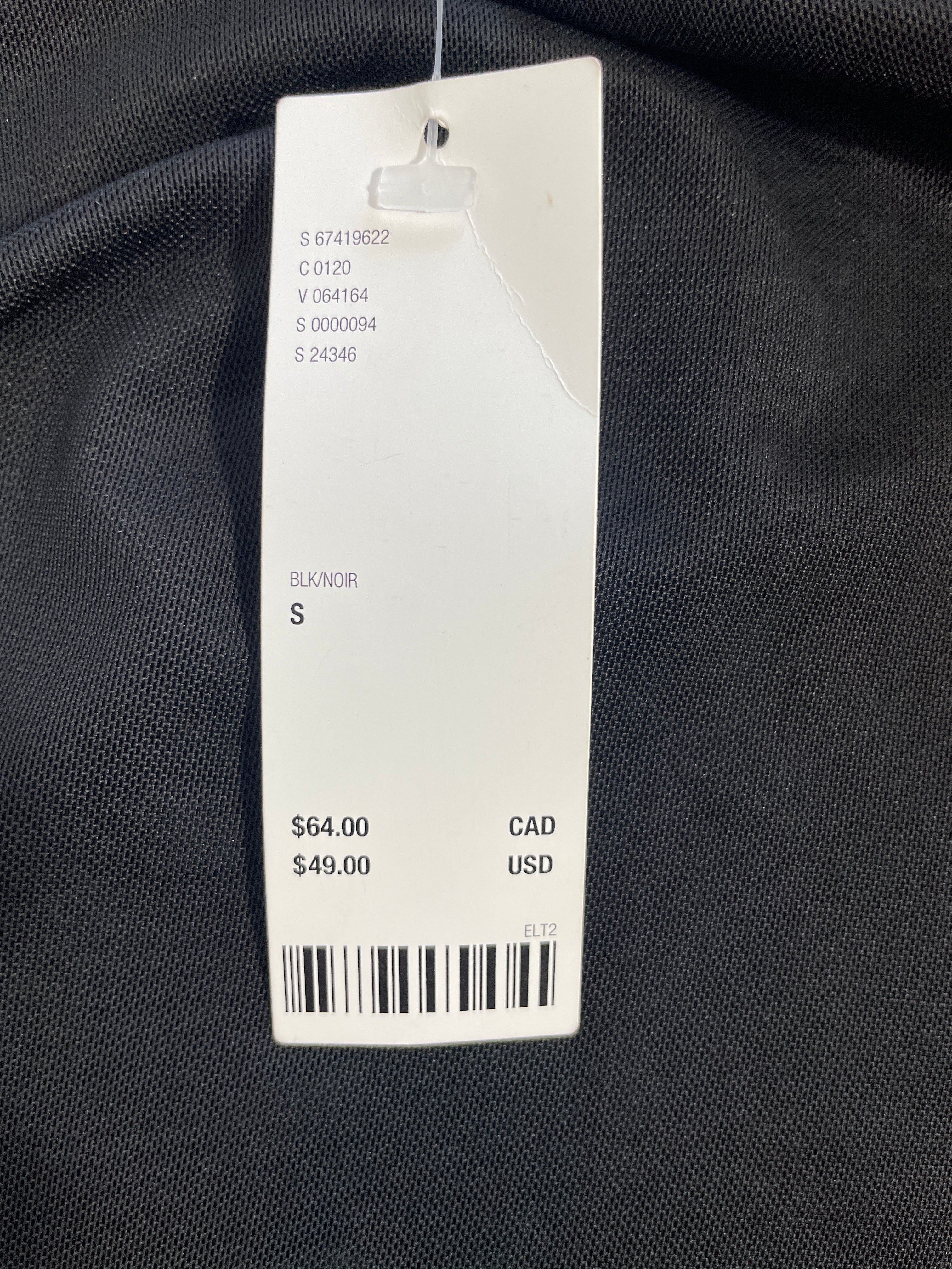 A white retail price tag with barcode and product info hanging on a black textured fabric garment.