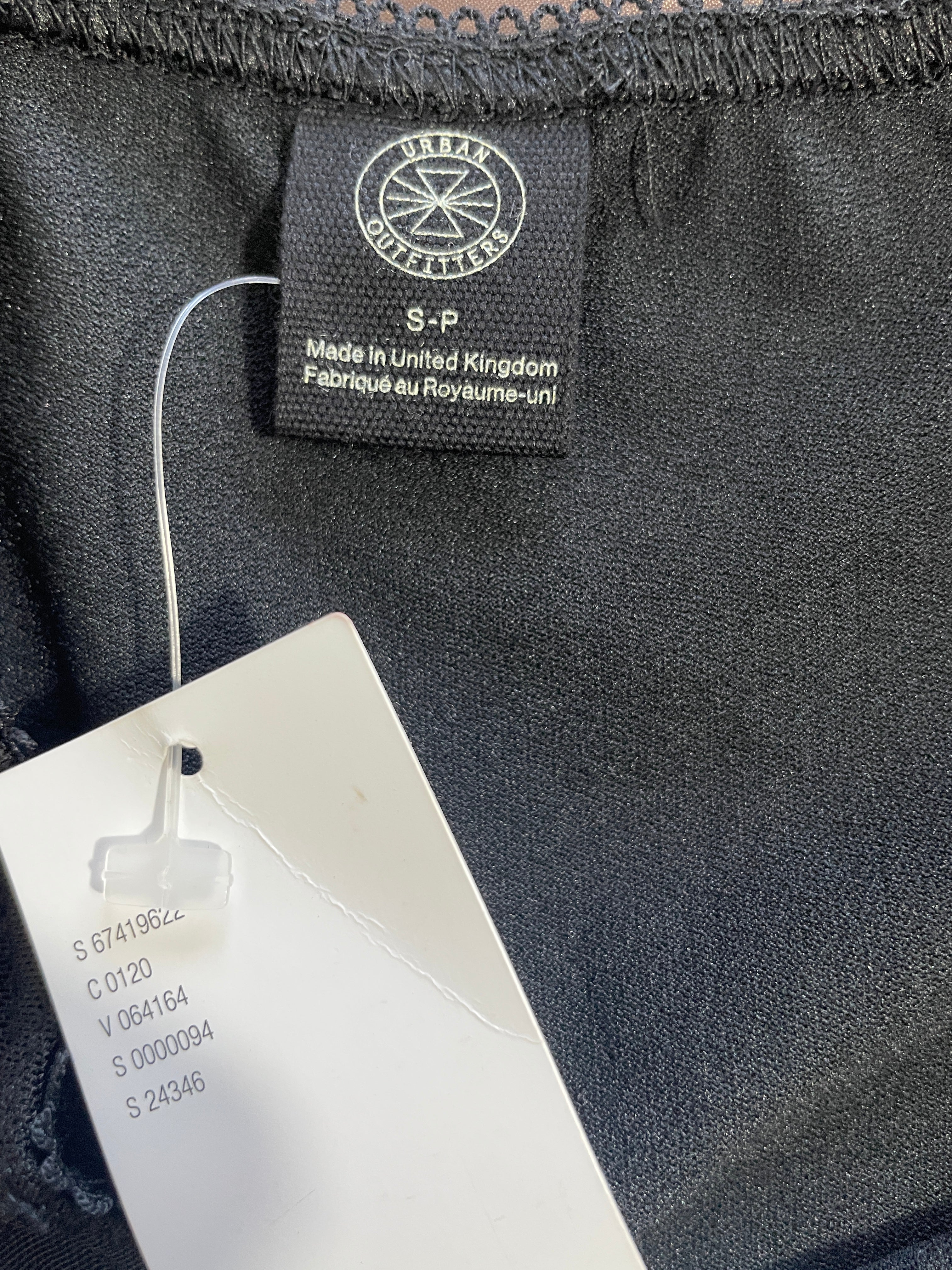 Close-up of a black garment label reading 'URMAN COLLECTIONS' with a white product tag attached, showing the inside neckline of a dark fabric item.