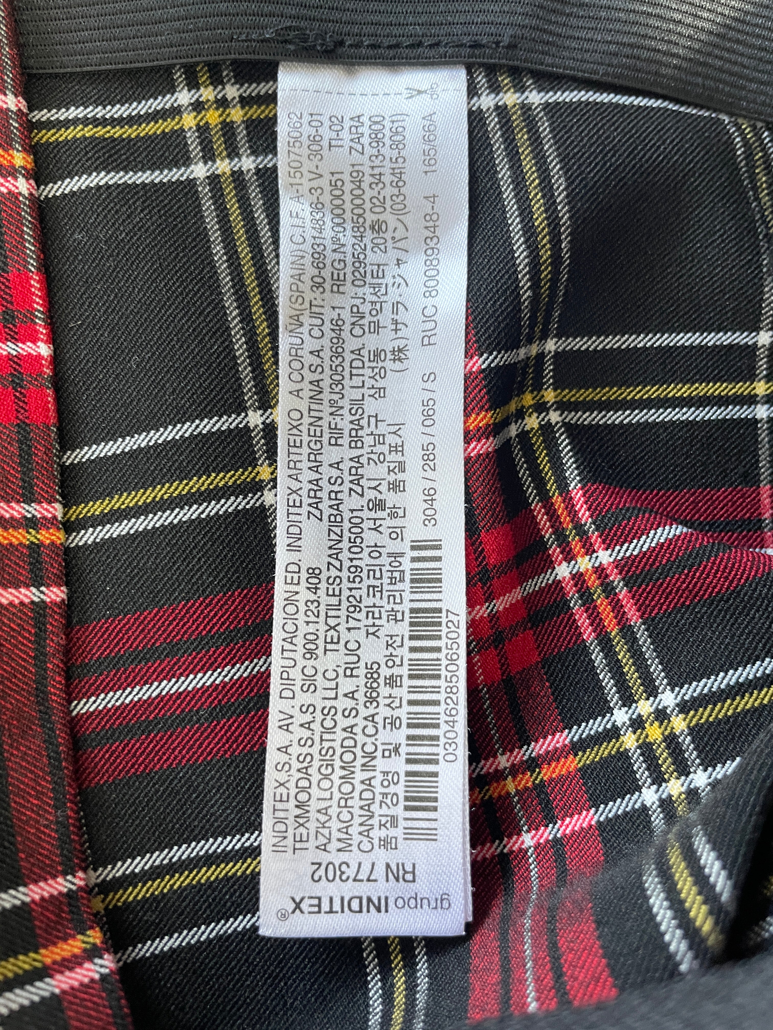 Close-up of a garment's interior label sewn onto a black, red, and yellow plaid fabric.