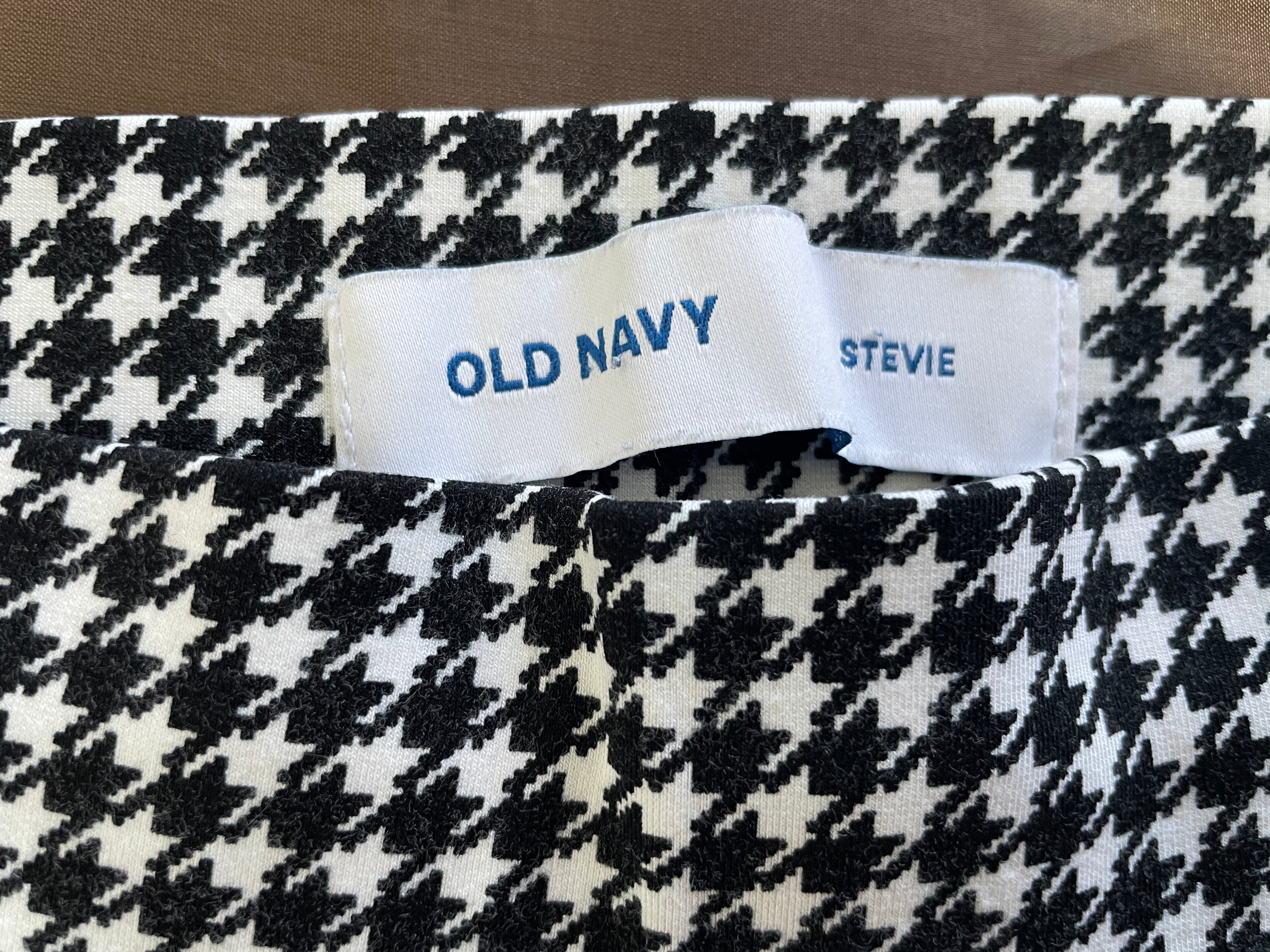 Close-up of a black and white houndstooth patterned fabric with a white Old Navy brand label sewn into the waistband.
