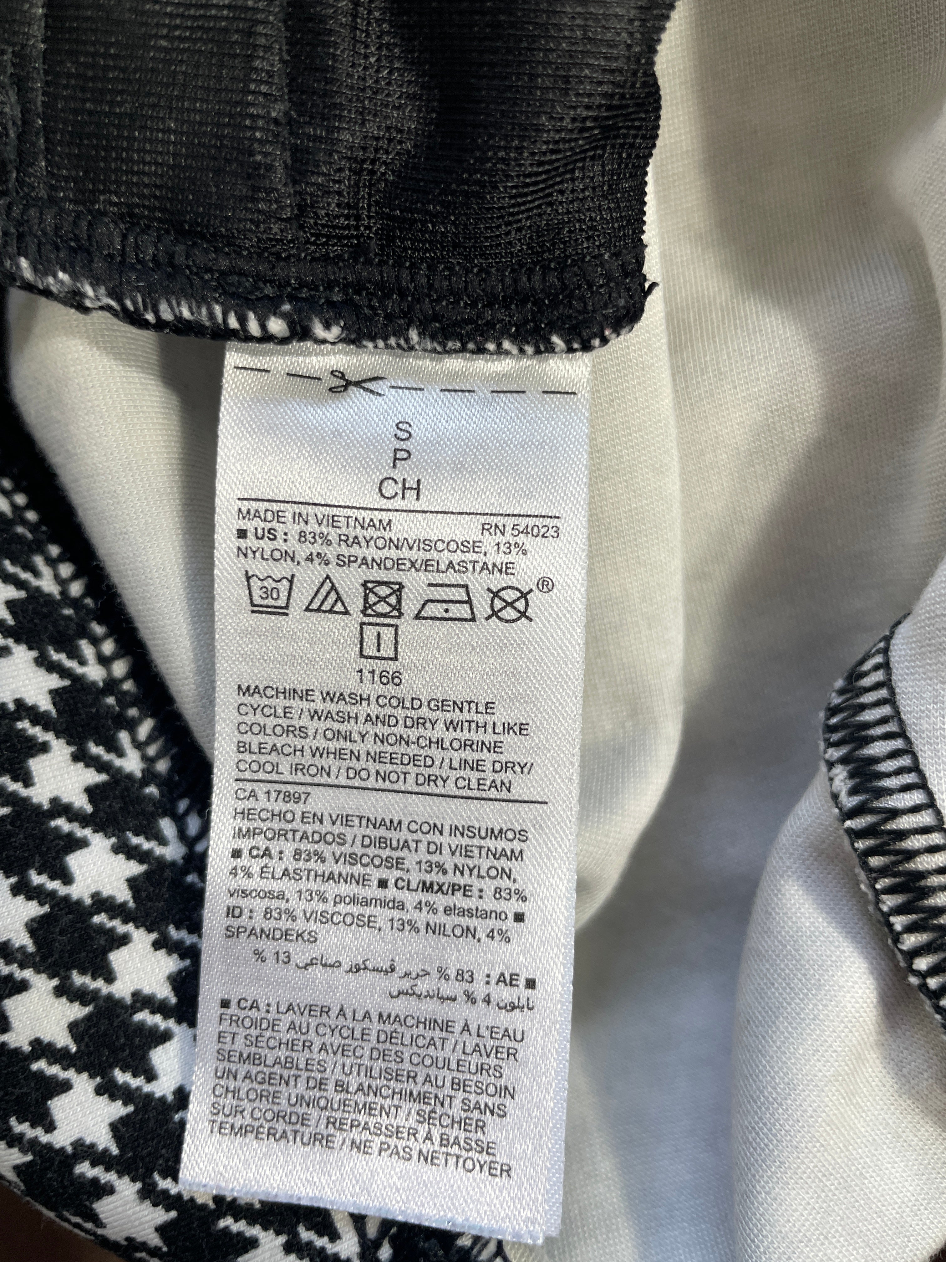 A close-up of a garment's interior neck label with care instructions and material composition, shown against black and white patterned fabric.
