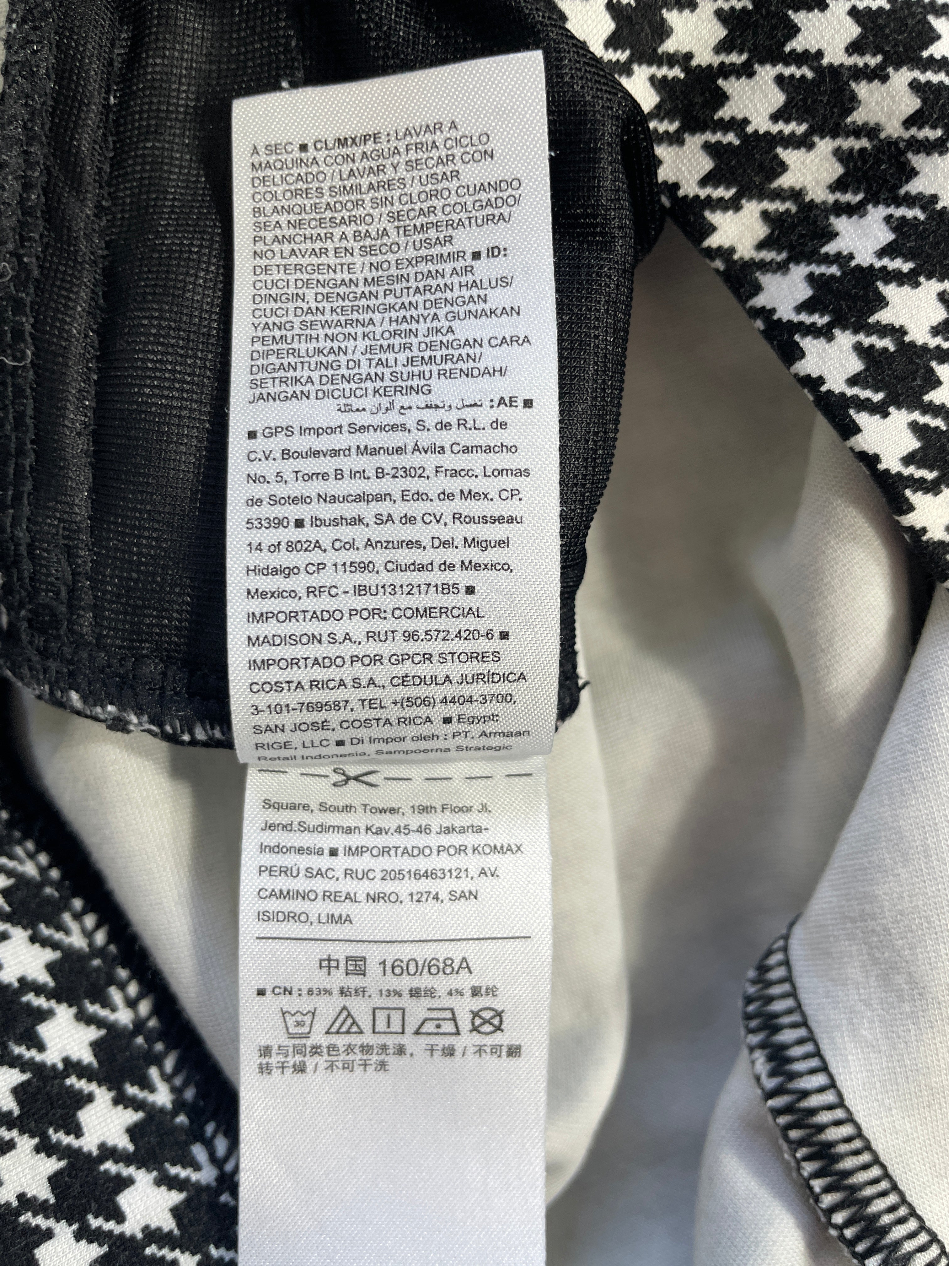 A close-up of a white garment care label sewn onto a black-and-white patterned fabric, showing printed text instructions and care symbols.