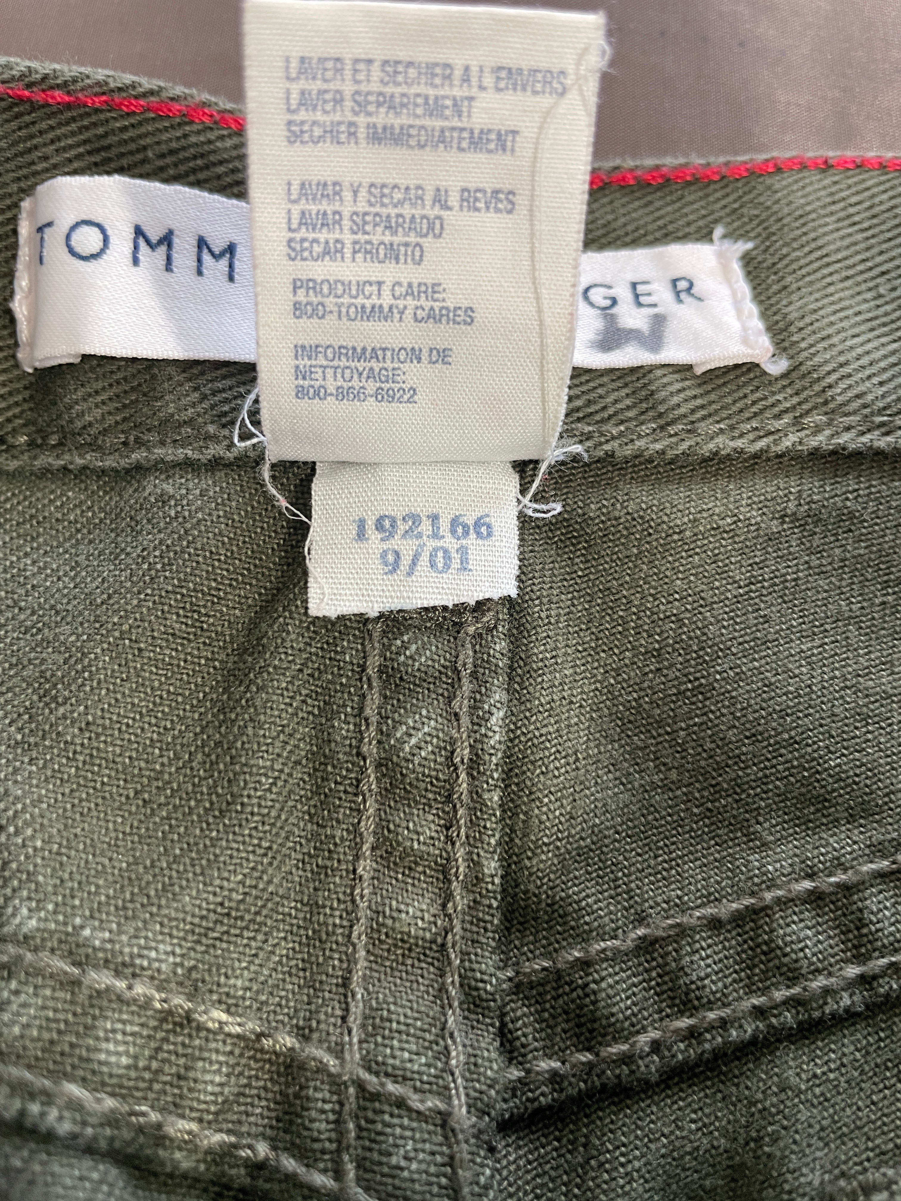 Close-up of the inner neck labels of olive green trousers, showing the brand TOMY and size information.