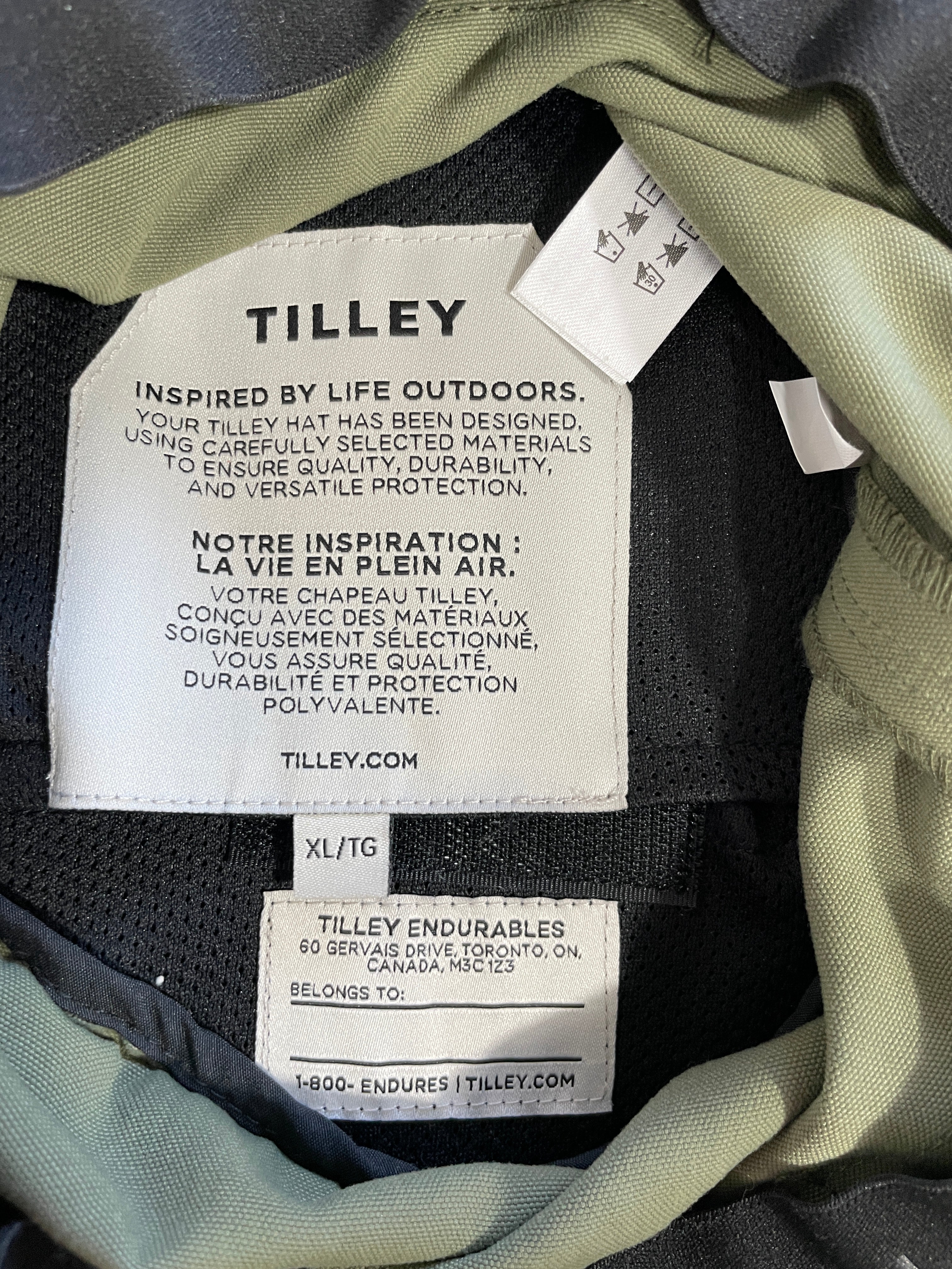 Close-up of the interior neck label of a Tilley Endurables jacket, showing the brand name 'TILLEY' and product details on a white tag over the dark gray fabric.