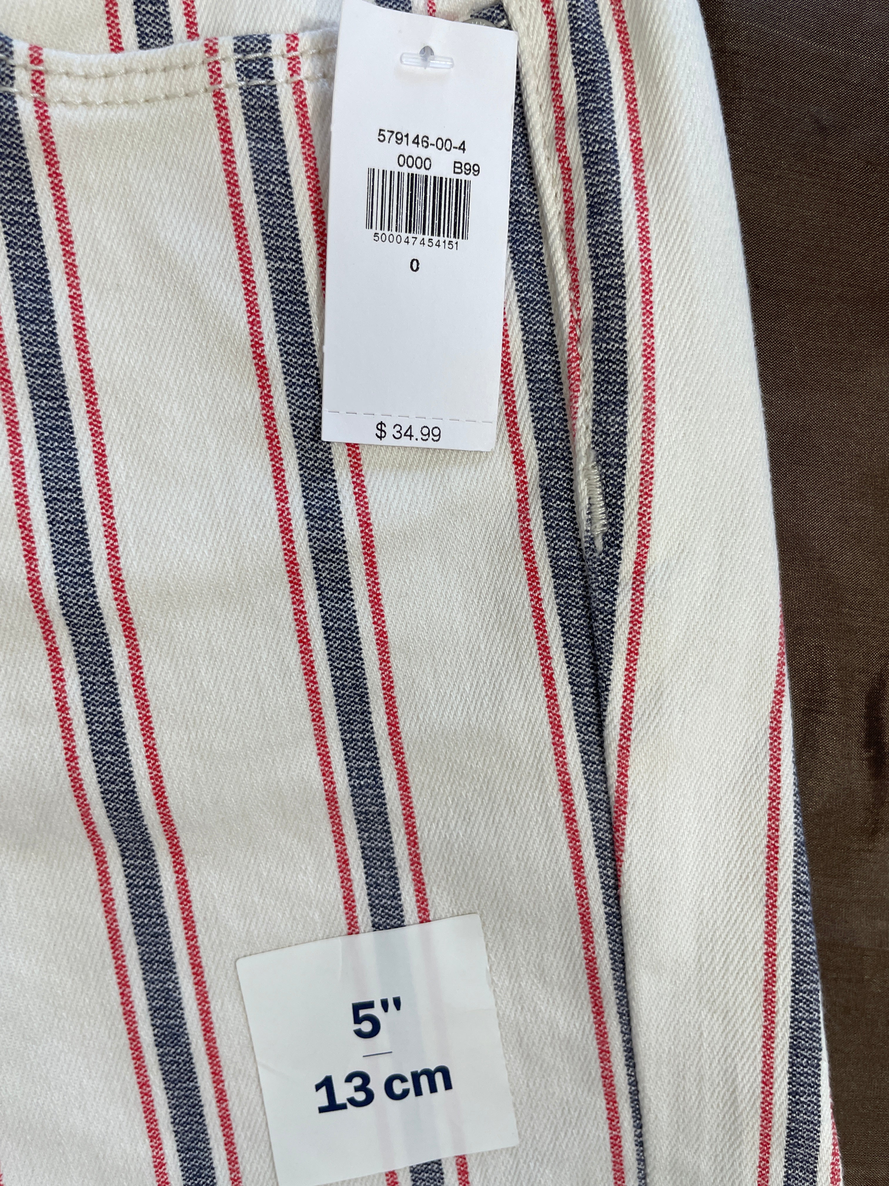 Close-up of striped fabric with a white price tag and a size label reading 5" / 13 cm, showing an off-white base with red and dark blue vertical stripes.