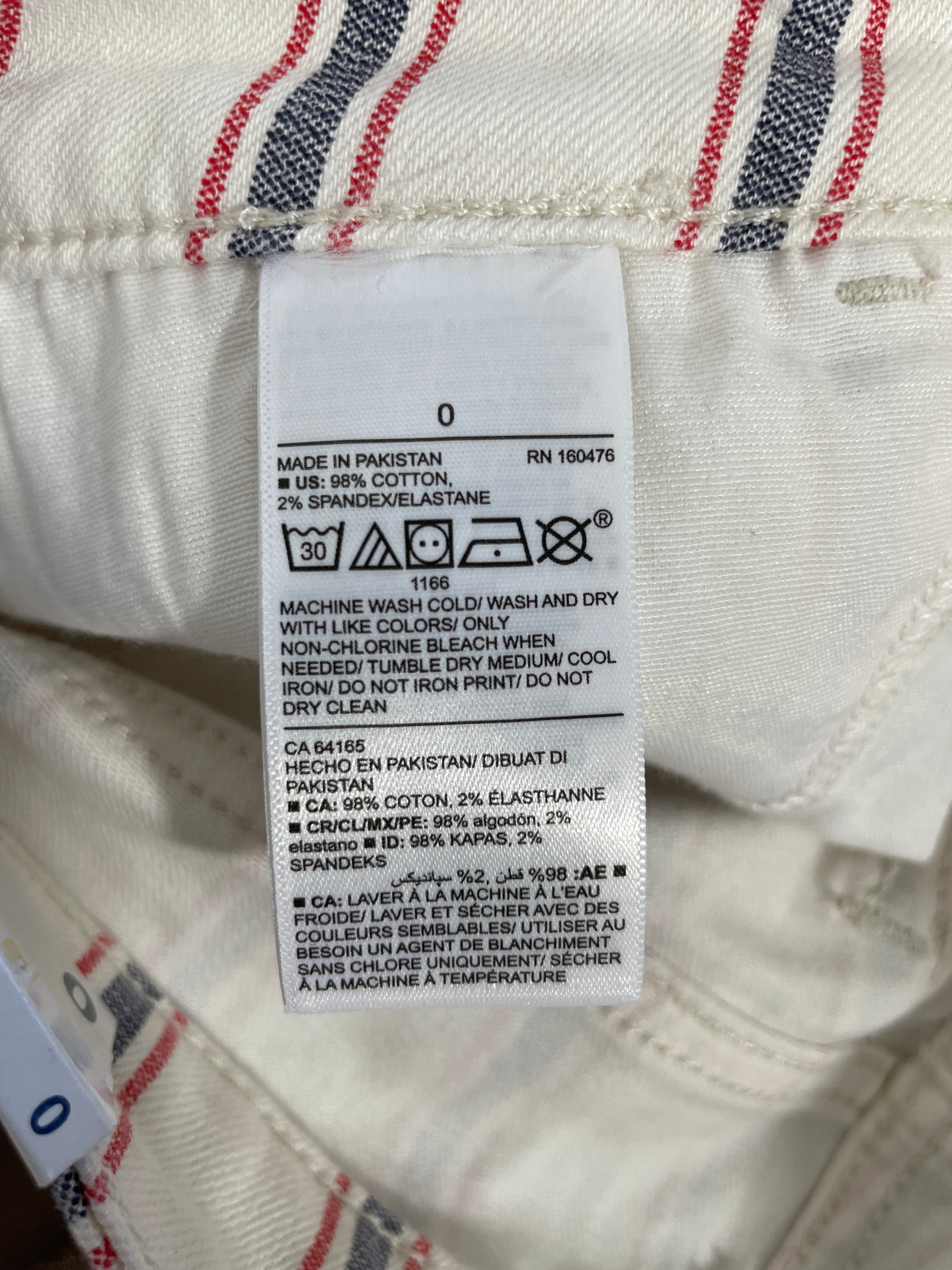 A close-up of a white garment label with printed care instructions and text, attached to a cream-colored plaid fabric garment.