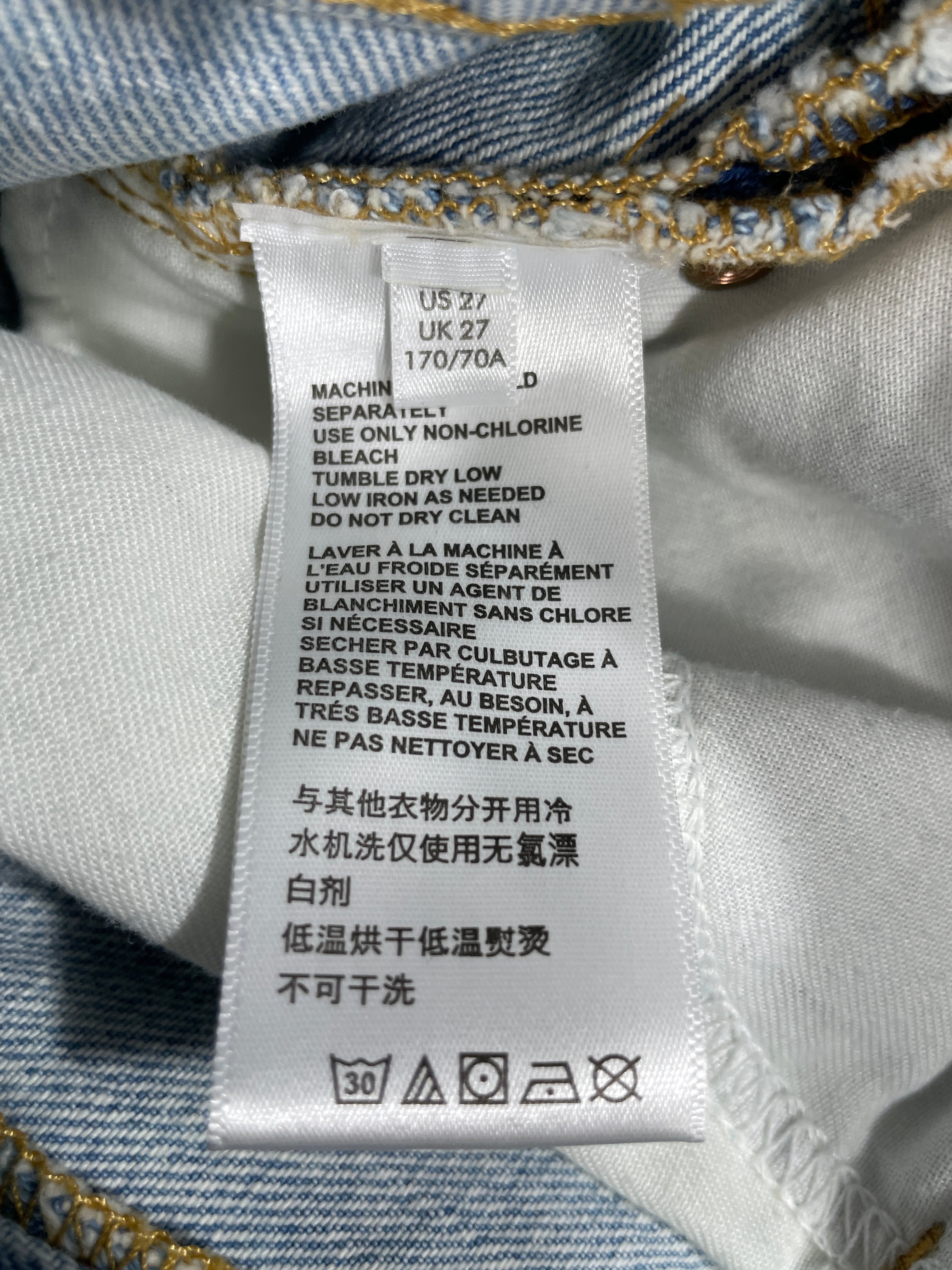 Close-up of a white garment care label sewn onto blue denim fabric, showing care instructions in English, French, and Chinese.