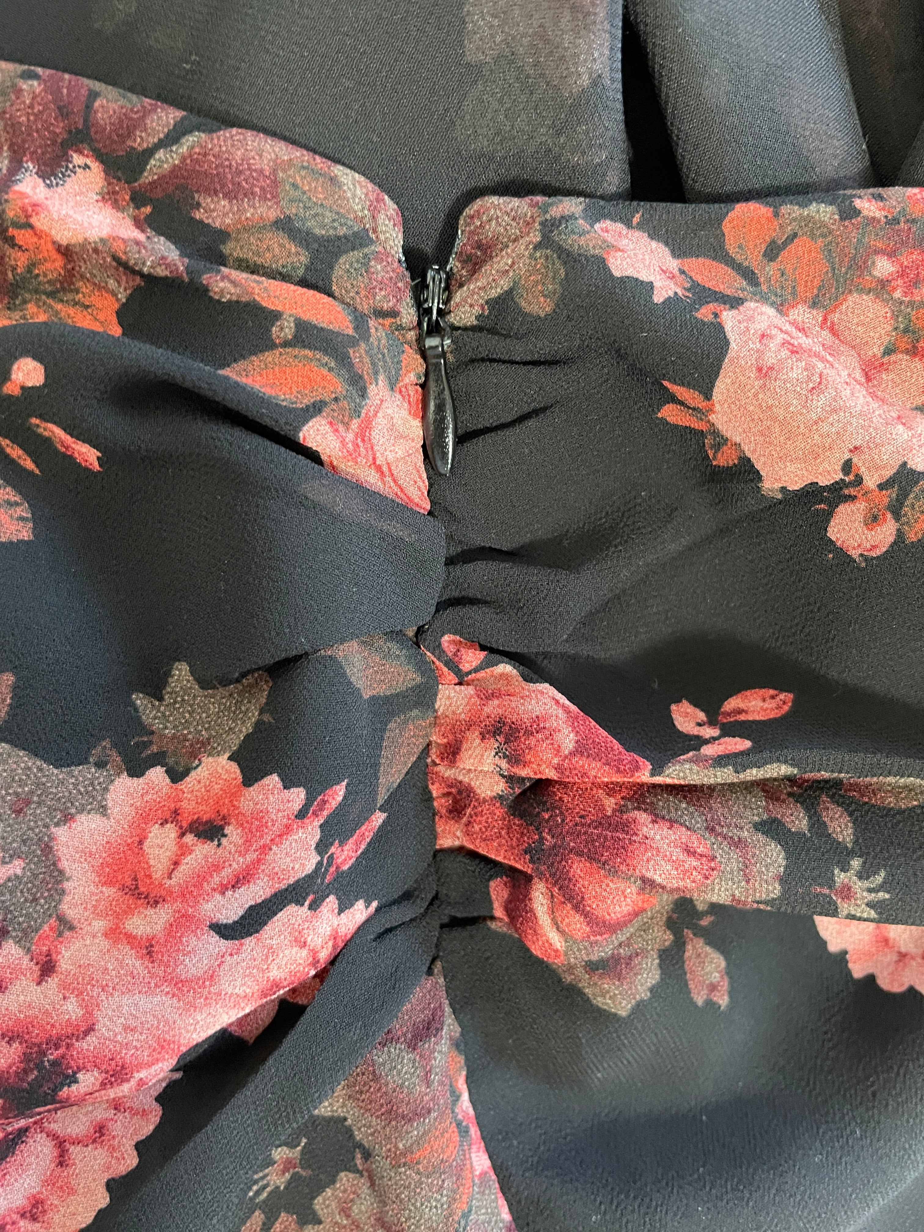 Close-up of a black fabric garment with a pink and red floral print, gathered at the center with a small dark zipper visible.