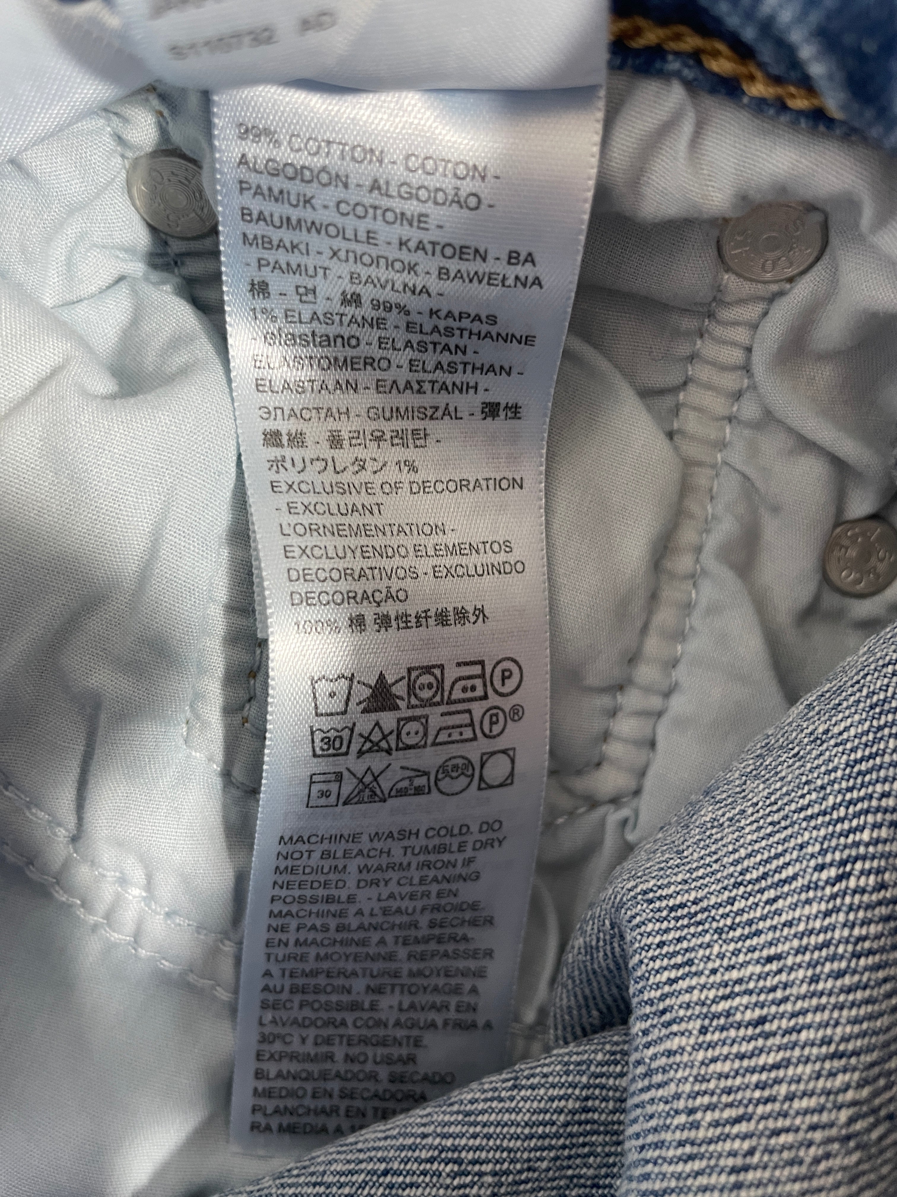 Close-up of a white garment care label sewn onto the inside collar of a blue denim jacket, showing fabric composition and care instructions.