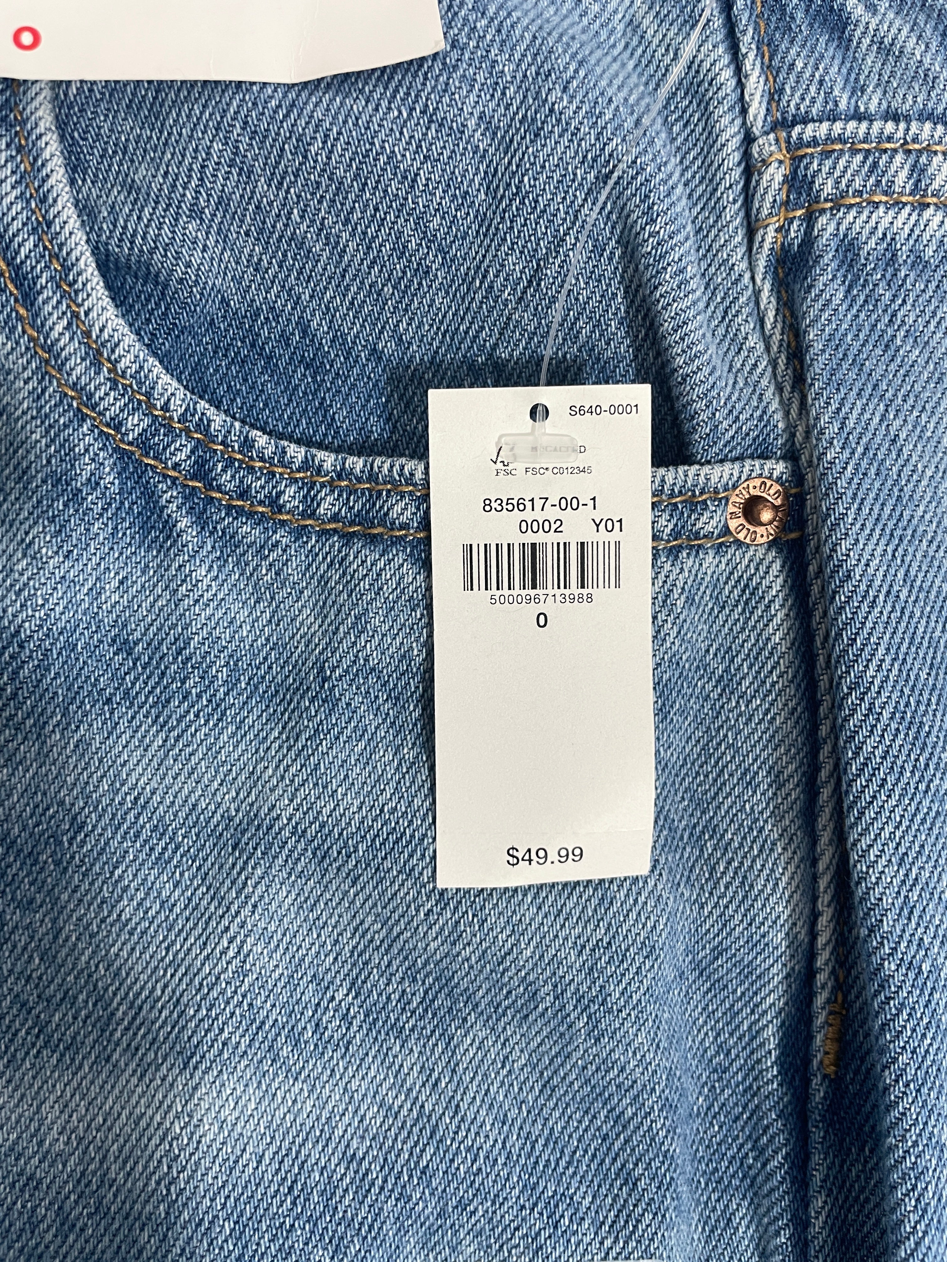 Close-up of a light blue denim jeans waistband with a white retail price tag attached near the buttonhole.