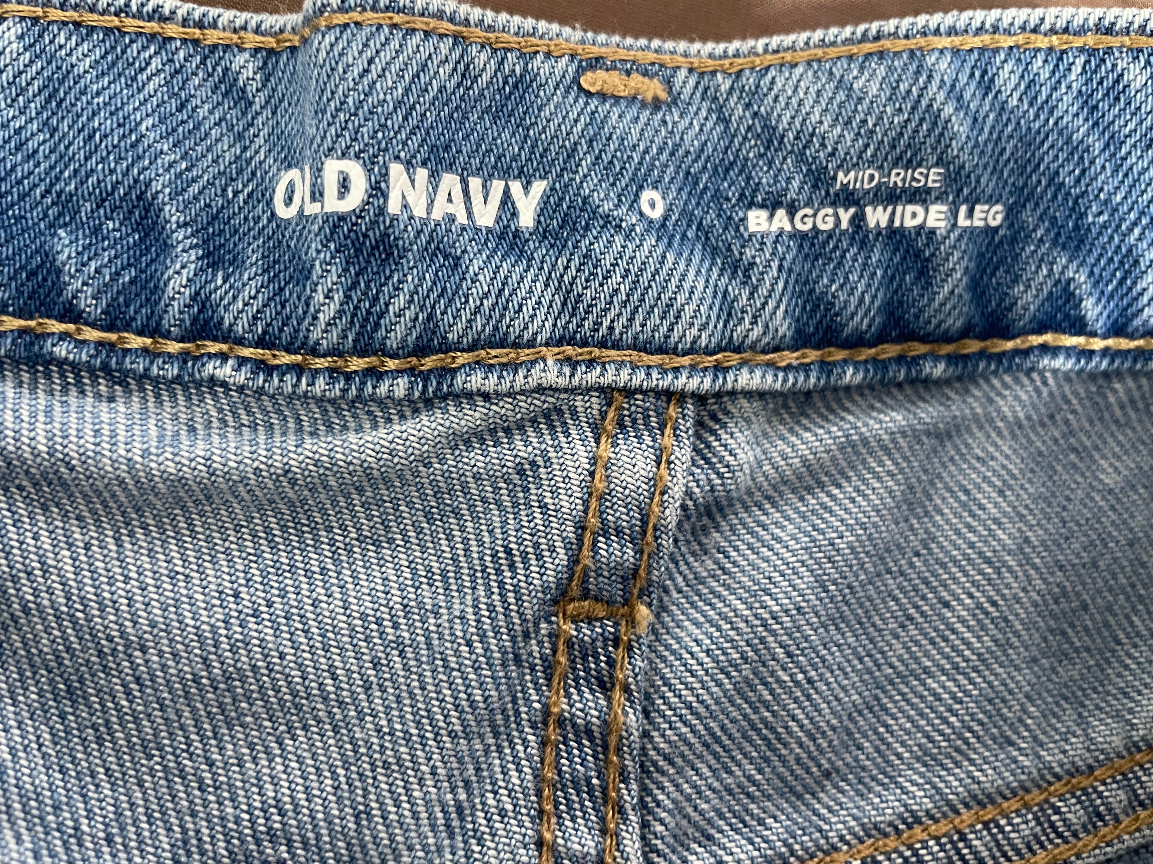 Close-up of the waistband of light-wash blue denim jeans showing the white printed Old Navy brand name and 'Mid-Rise Baggy Wide Leg' text.