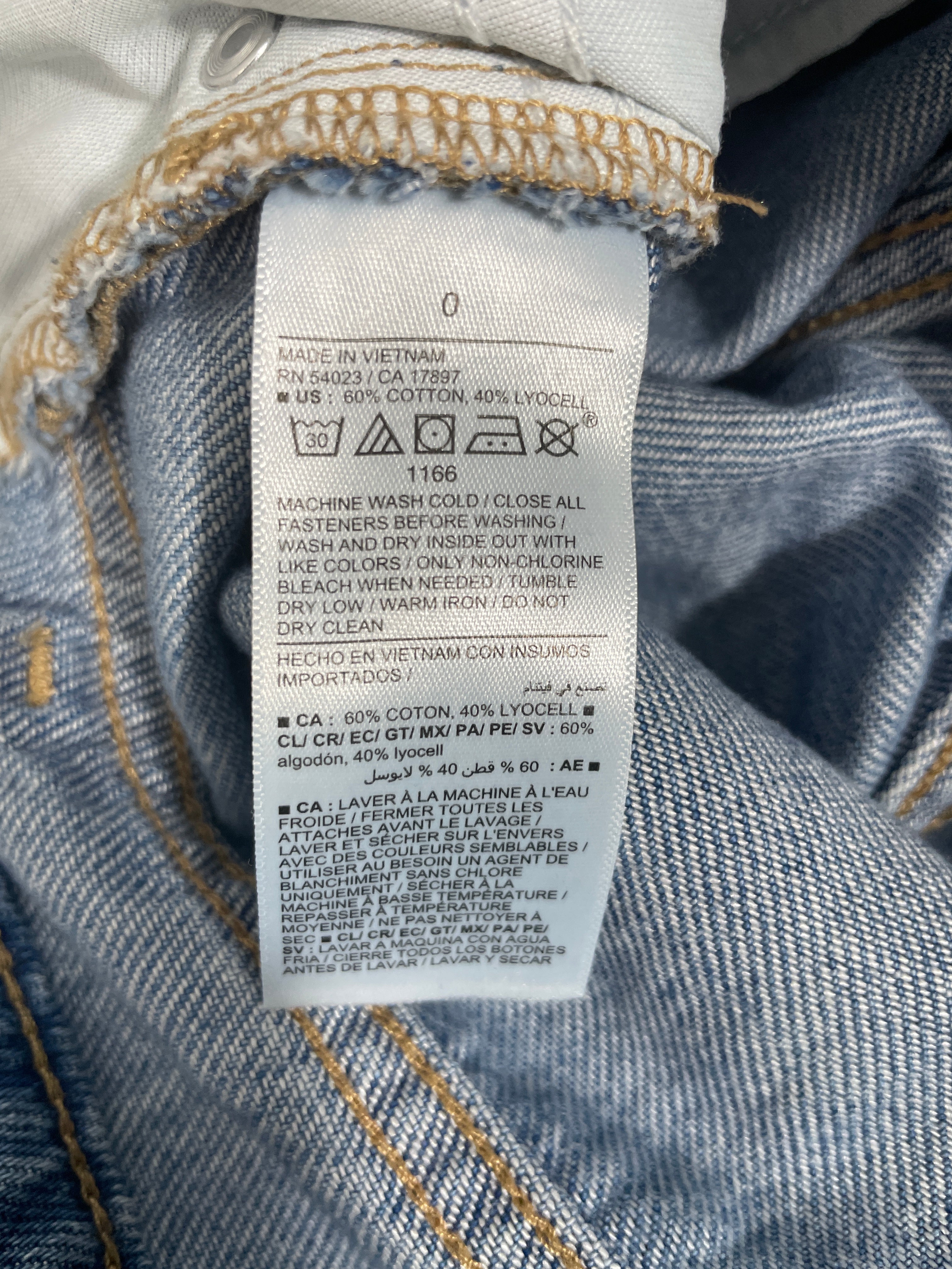 Close-up of a white garment care label sewn onto blue denim fabric, showing text including care symbols and material information.