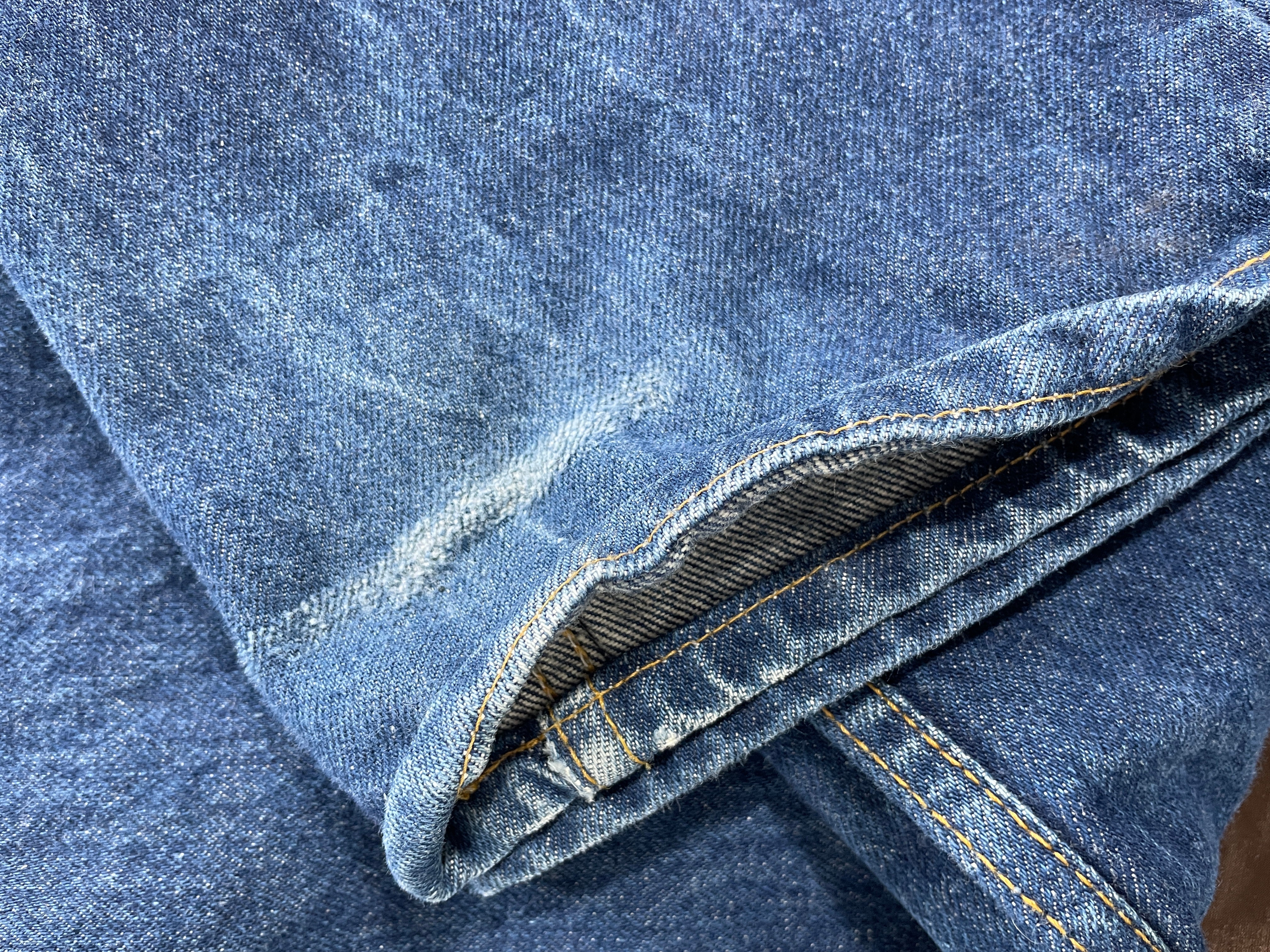 Close-up of blue denim fabric with visible stitching and a folded corner showing the inner denim weave.