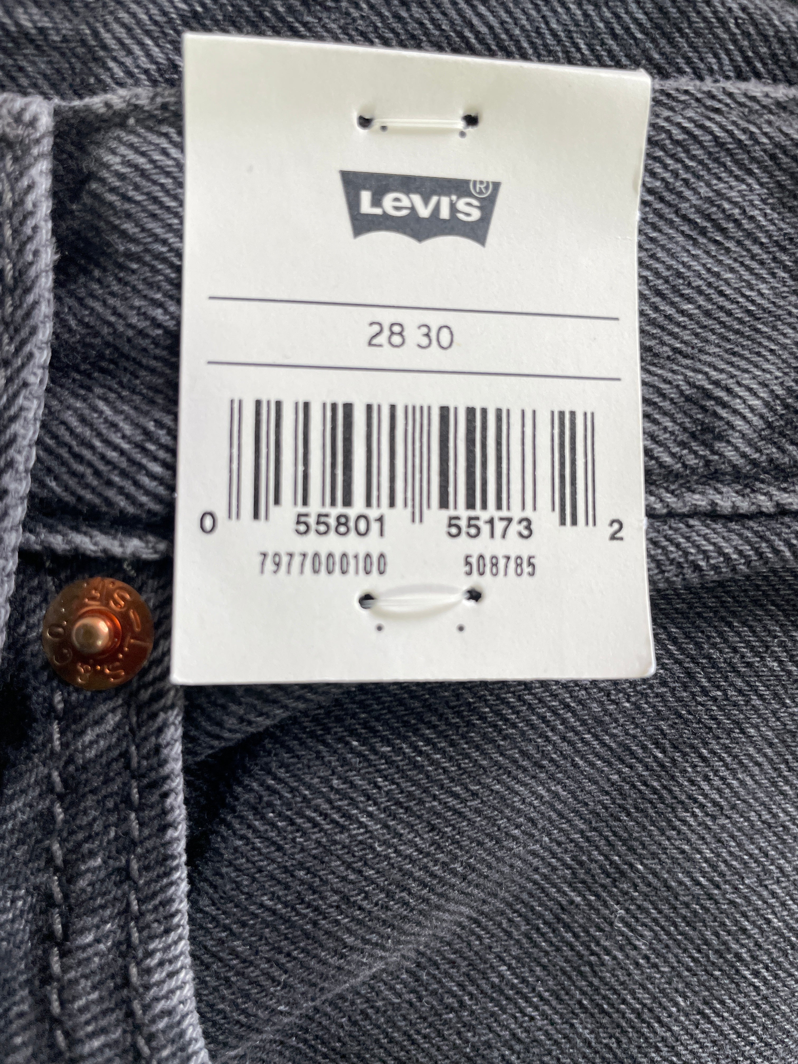 Close-up of Levi's denim jeans showing a white size tag with barcode and size 28 30, alongside a brown button on dark blue denim.