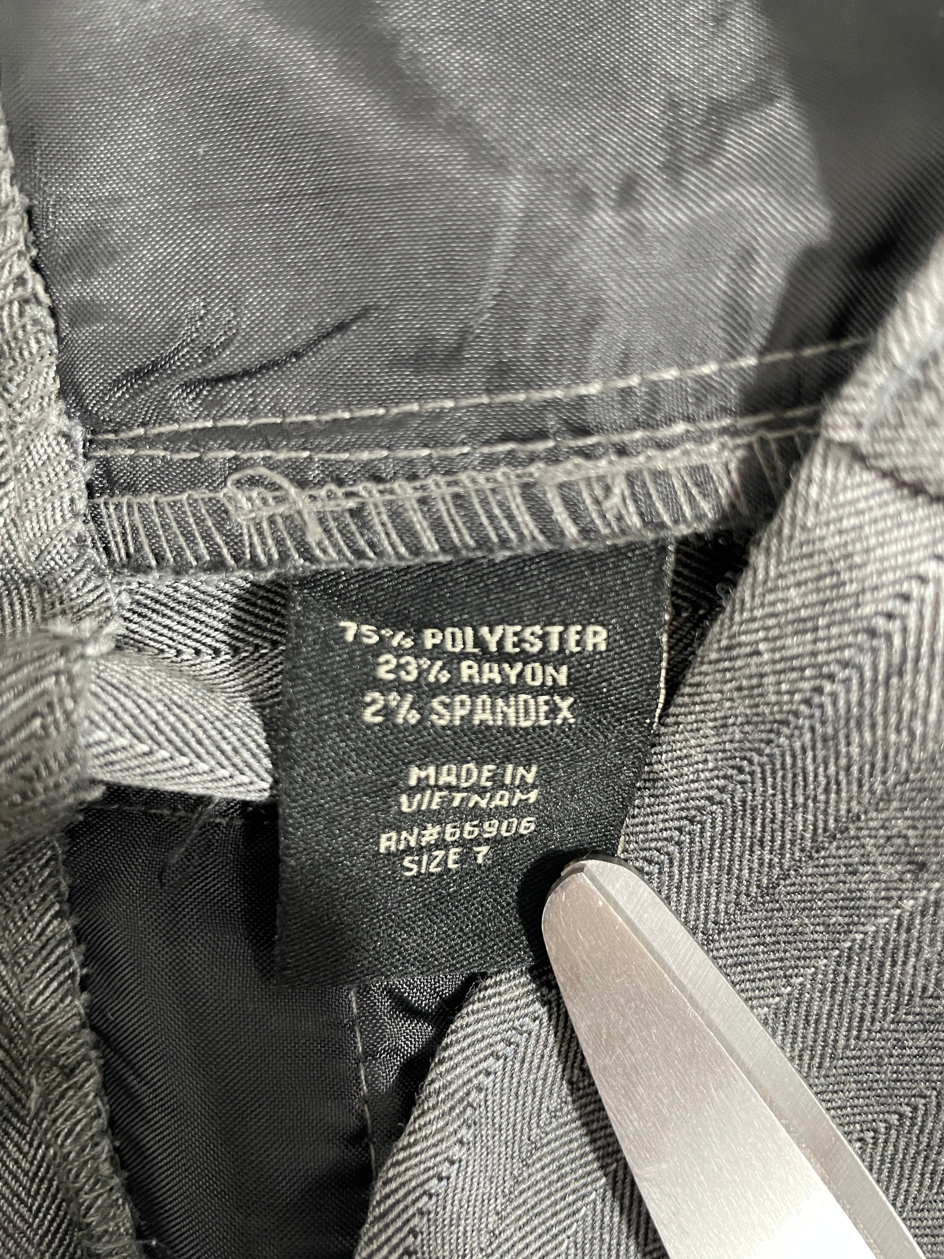 Close-up of a garment's interior label showing the brand 'TSA' and material composition of 75% polyester, 25% spandex, with a metal tool touching the collar.