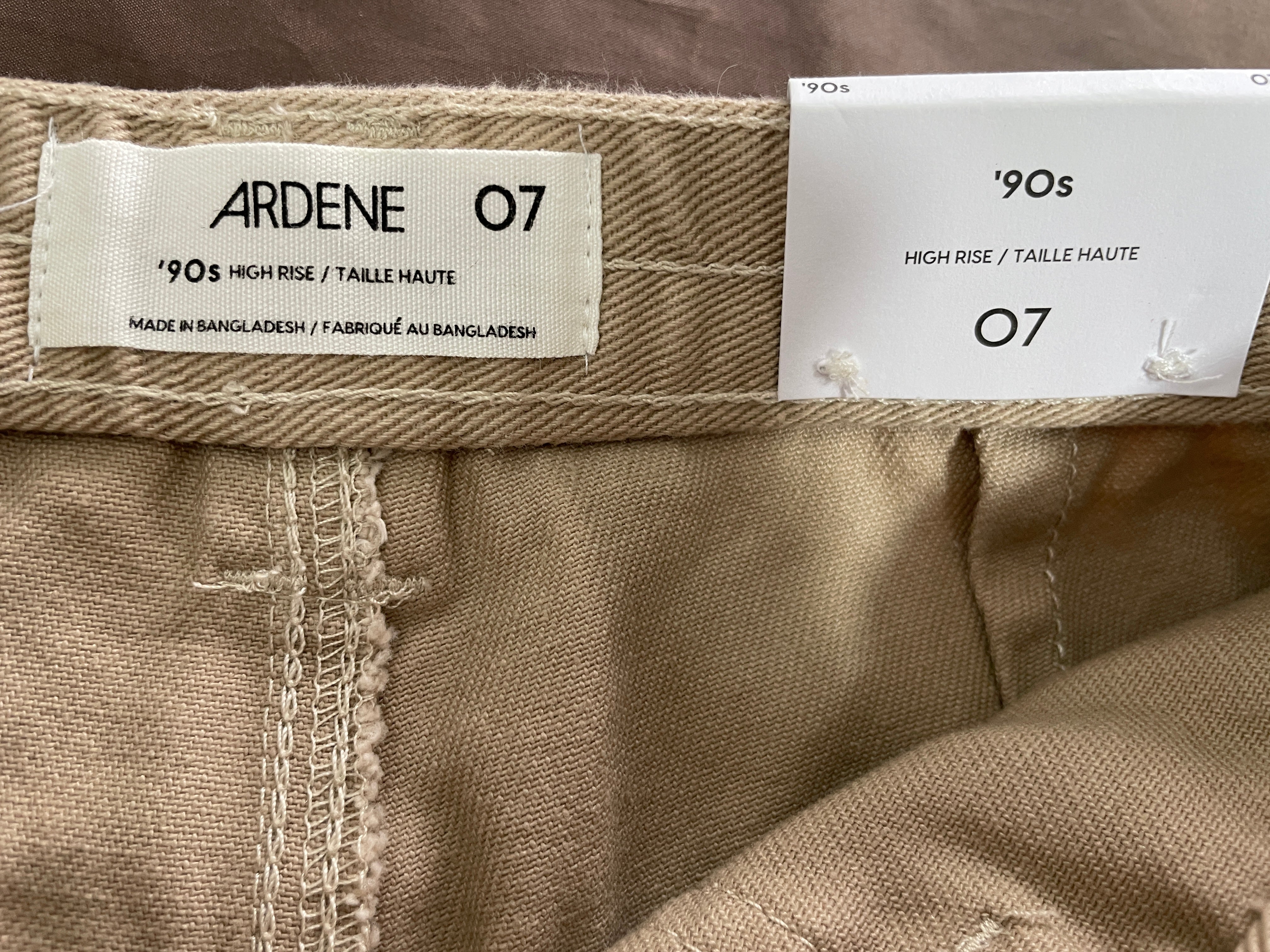 Close-up of the waistband of a pair of beige high-rise trousers, showing the Ardene brand label and the size '07' tag.