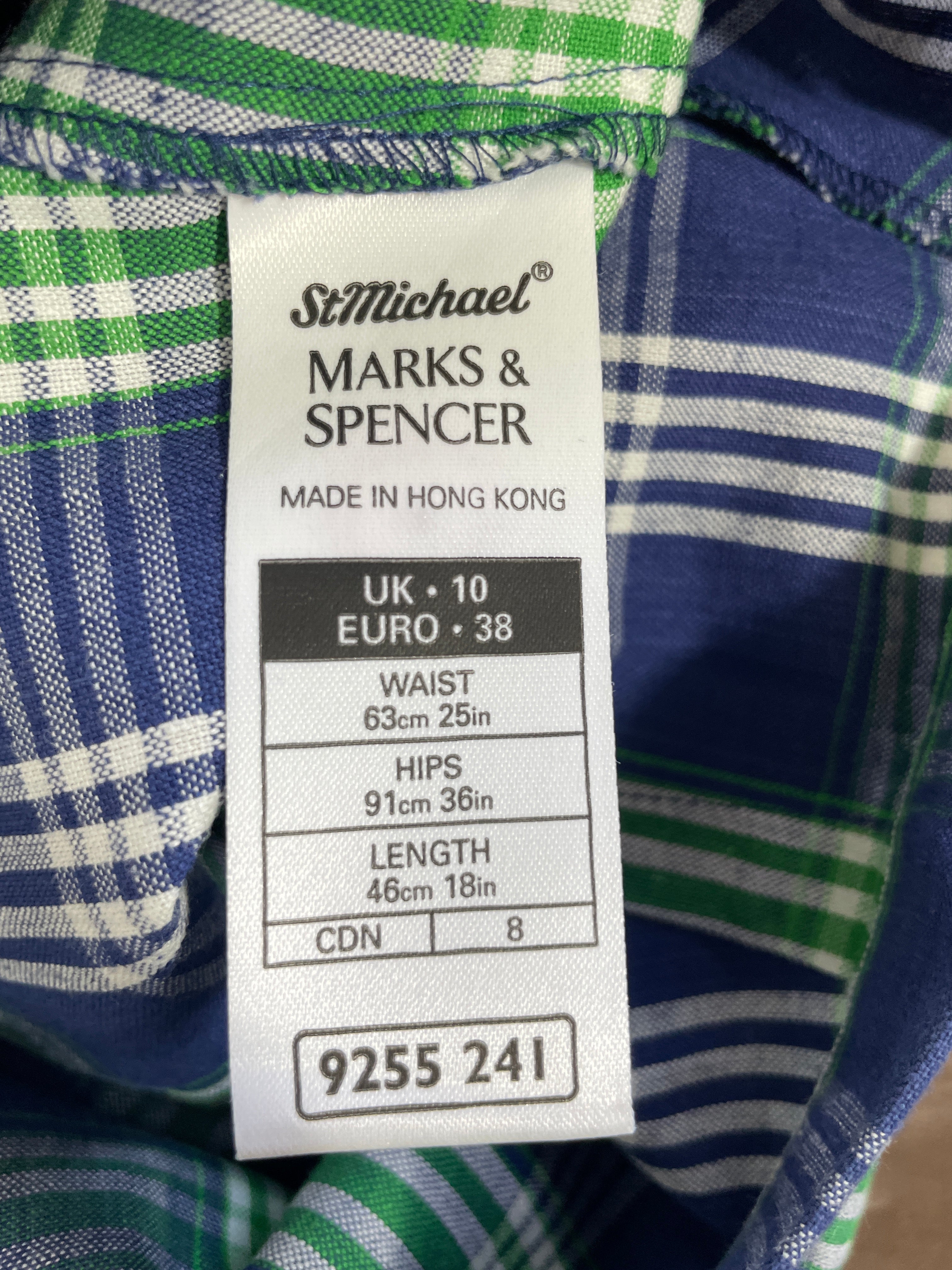 Close-up of a garment's interior label reading 'StMichael MARKS & SPENCER' with size information and measurements, shown against blue, green, and white plaid fabric.