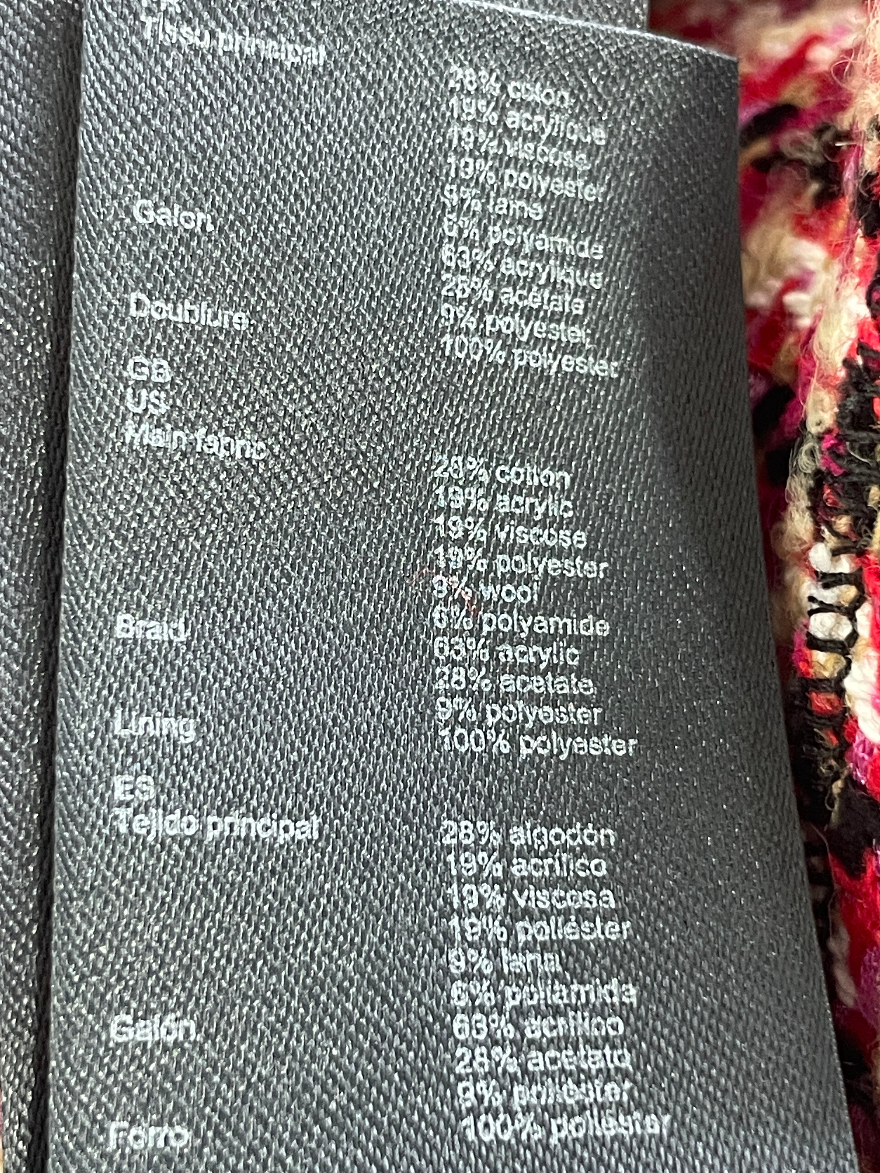 Close-up of a black textured garment tag with white printed material composition and fabric percentages, placed on a colorful knitted blanket.