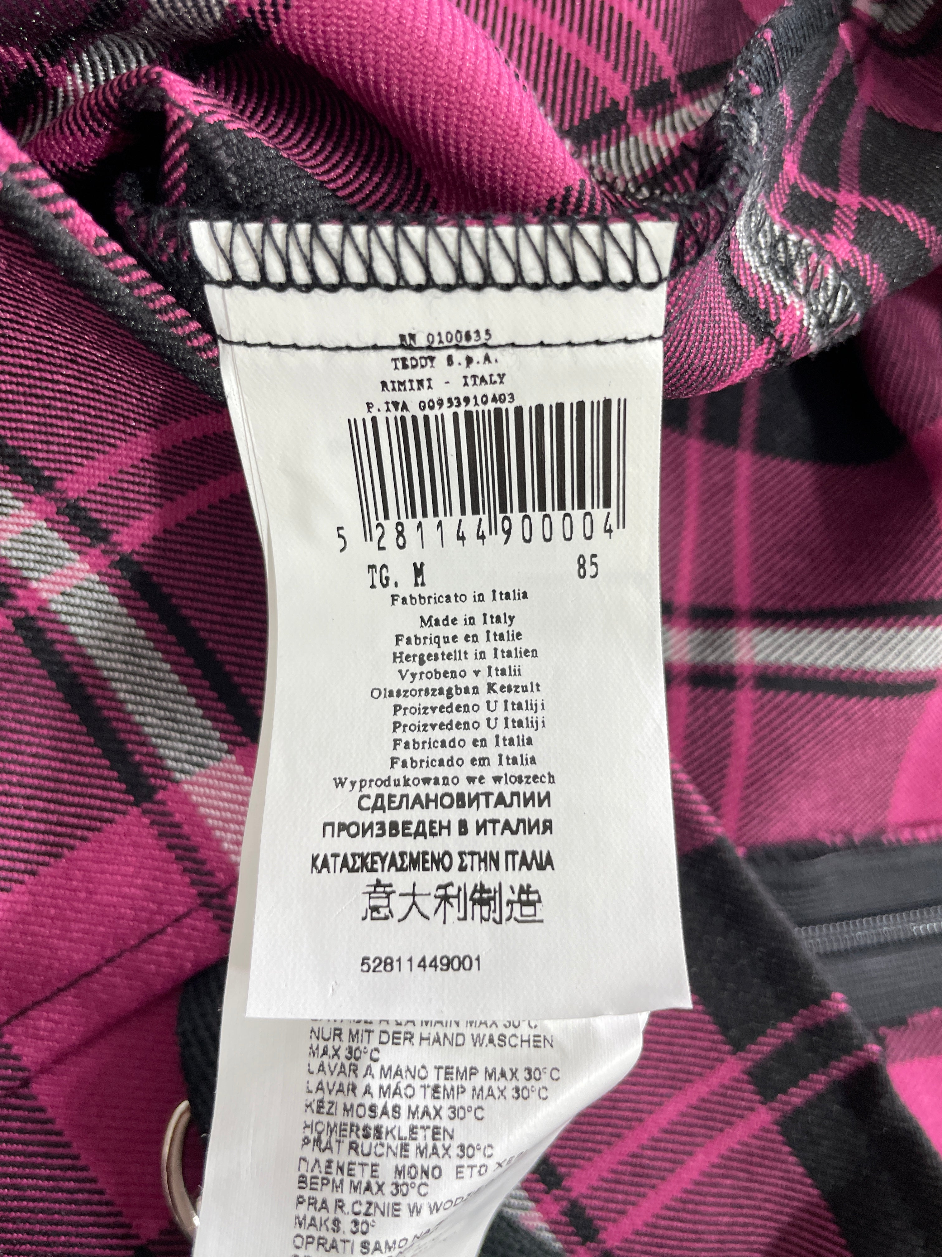 A close-up of a garment's interior label sewn onto a pink and black plaid fabric, showing barcode details and care instructions.