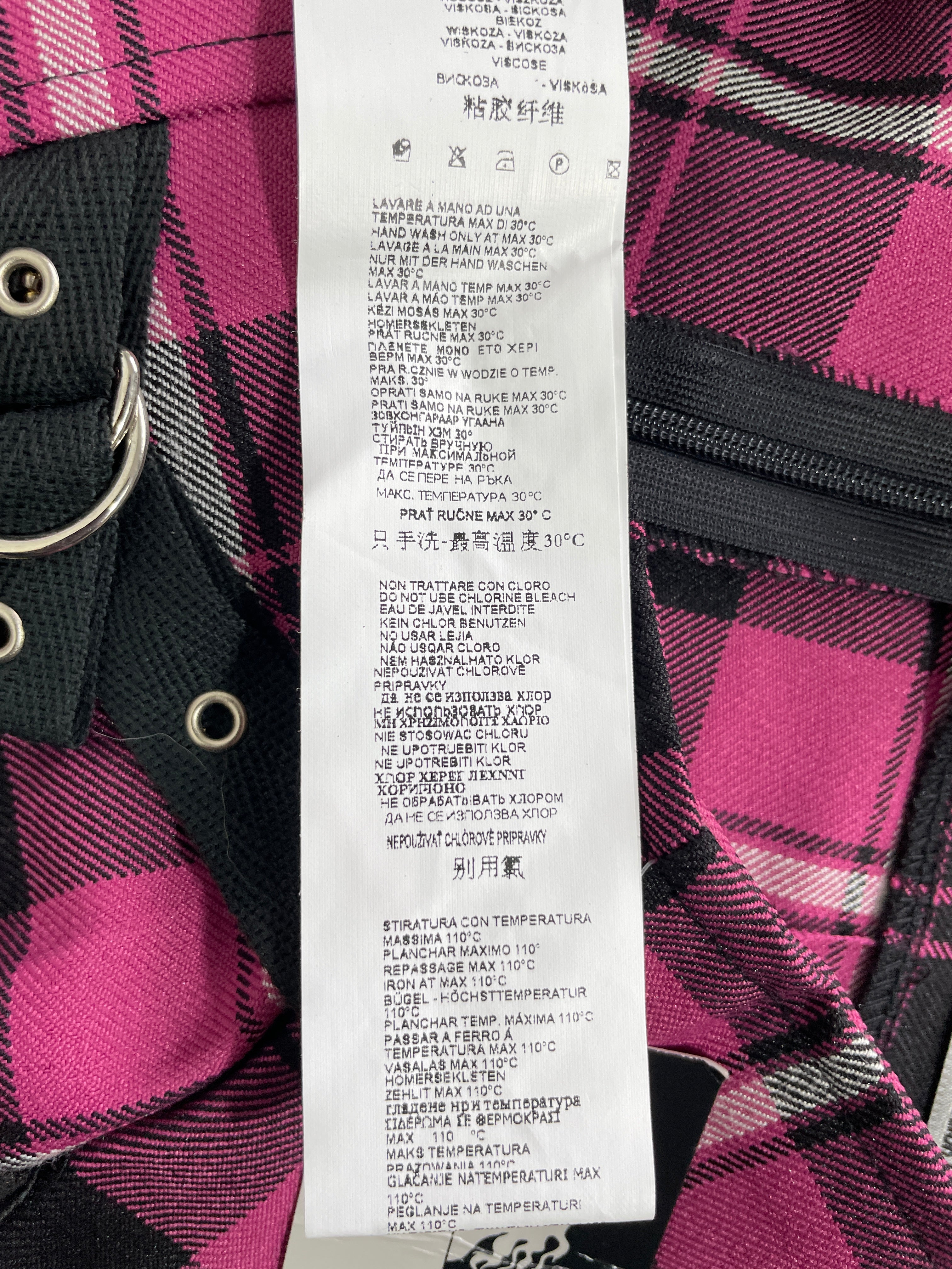 A close-up of a pink and black plaid garment with a white laundry care label attached, showing text instructions in multiple languages.