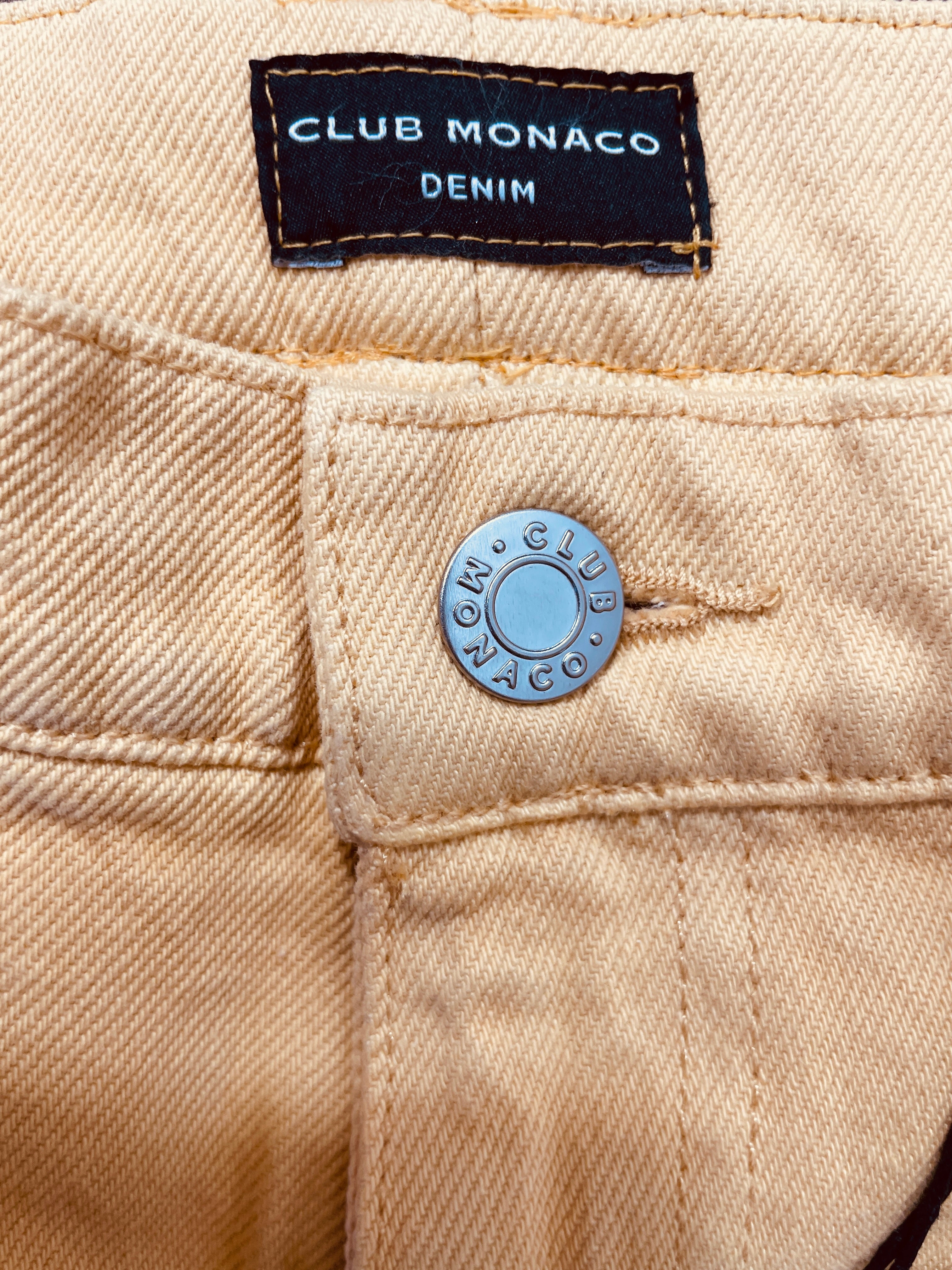 Club Monaco Denim label and branded metal button on mustard yellow jeans