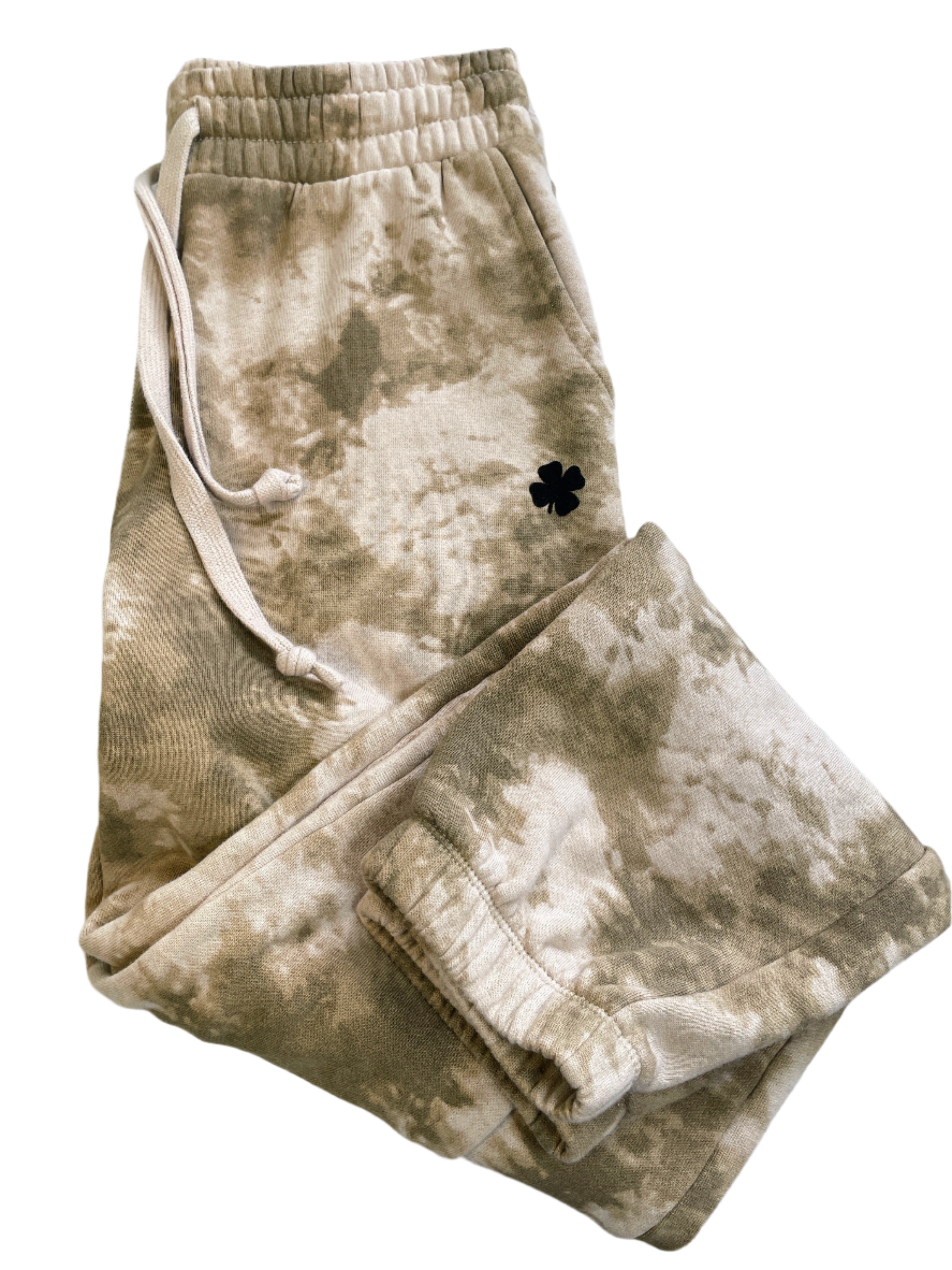 Beige tie-dye sweatpants with a black four-leaf clover patch on a white surface.