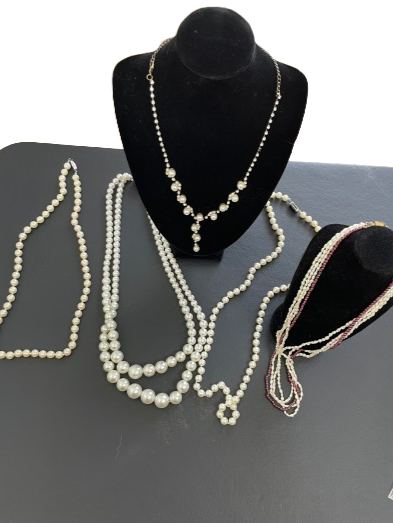 Set of five costume pearl necklaces including rhinestone-accented, multi-strand, double strand, and two single strands displayed on black necklace stands.
