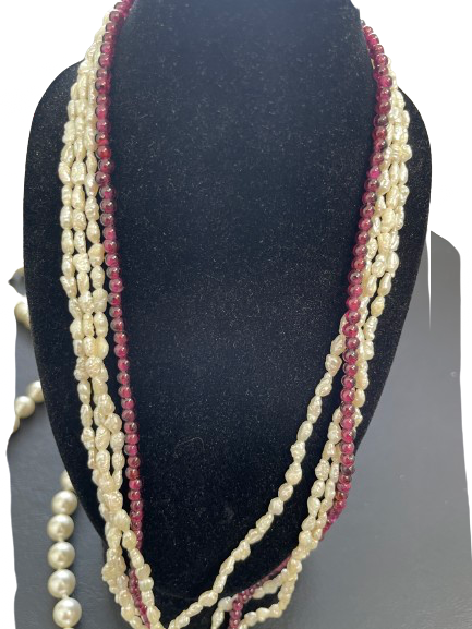 Multi-strand pearl and red bead necklace on a black mannequin bust.