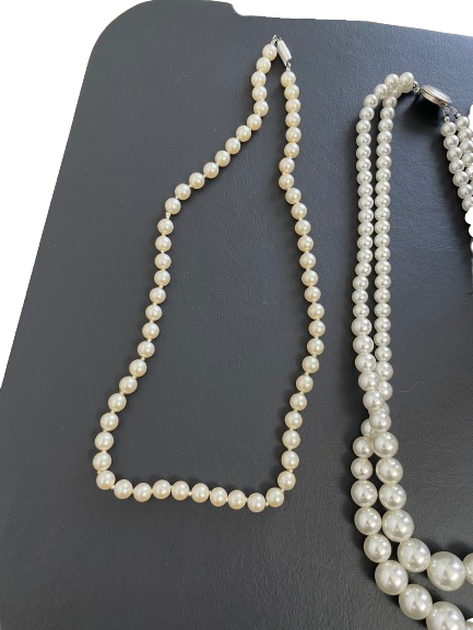 Two pearl necklaces on a dark surface
