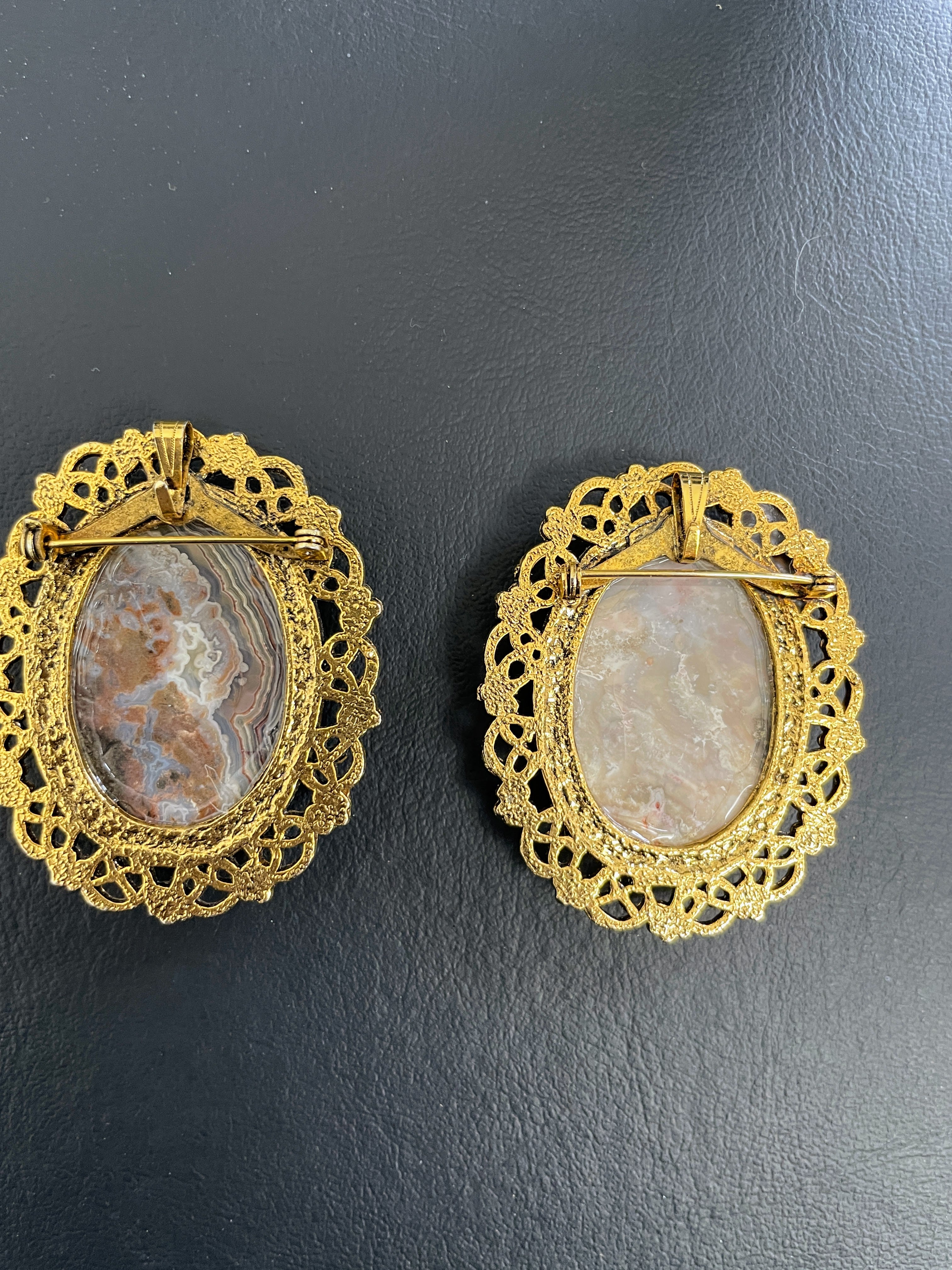 Pair of gold-framed stone brooches on a dark background