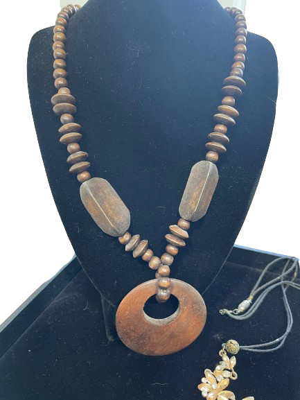 Wooden beaded necklace with a large circular pendant on a black stand.