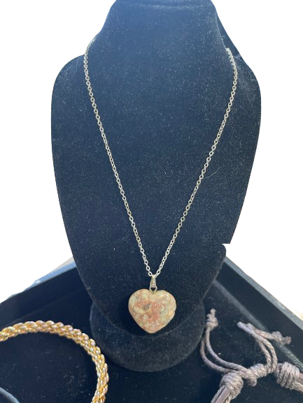 Heart-shaped pendant necklace on a blue velvet stand with a gold bracelet and white rope on a white background