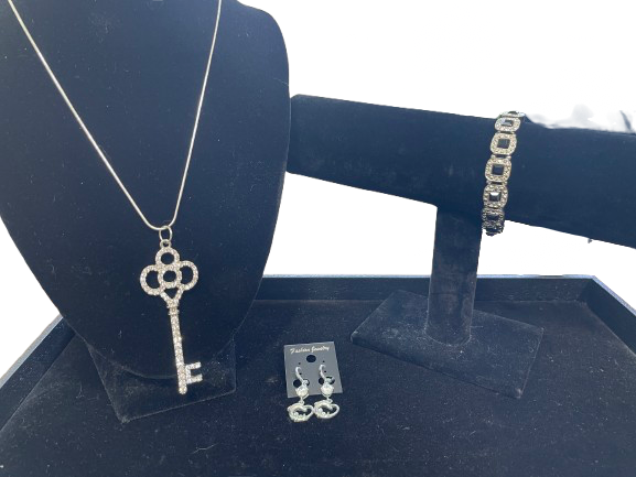 Jewelry set including a key-shaped pendant, bracelet, and earrings on a blue stand.