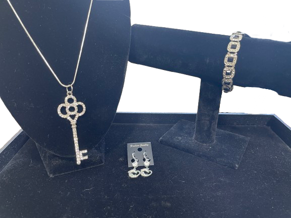 Jewelry set including a key-shaped pendant, bracelet, and earrings on a black stand.