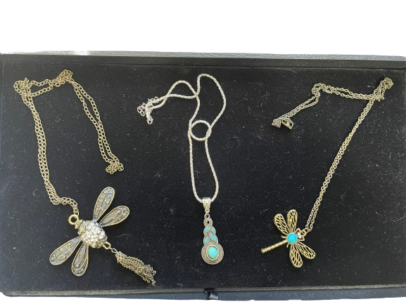 Three gold necklaces with dragonfly pendants on a black display stand.