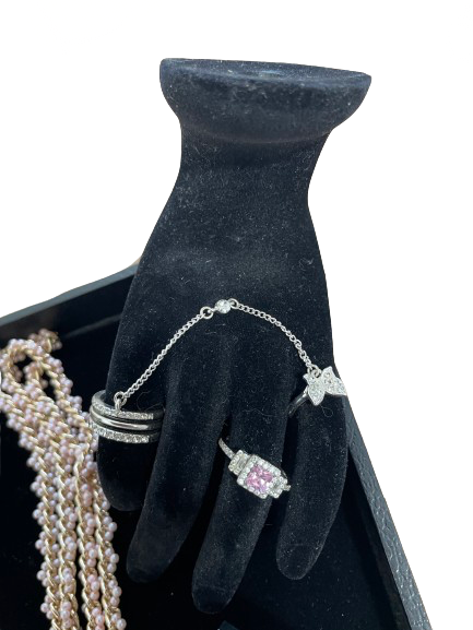 Black jewelry display with rings and a necklace on a white background