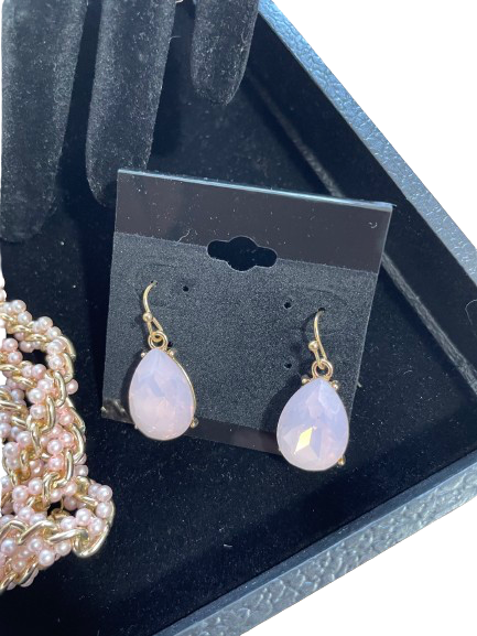 Teardrop-shaped earrings on a black card with a pearl necklace in the background.
