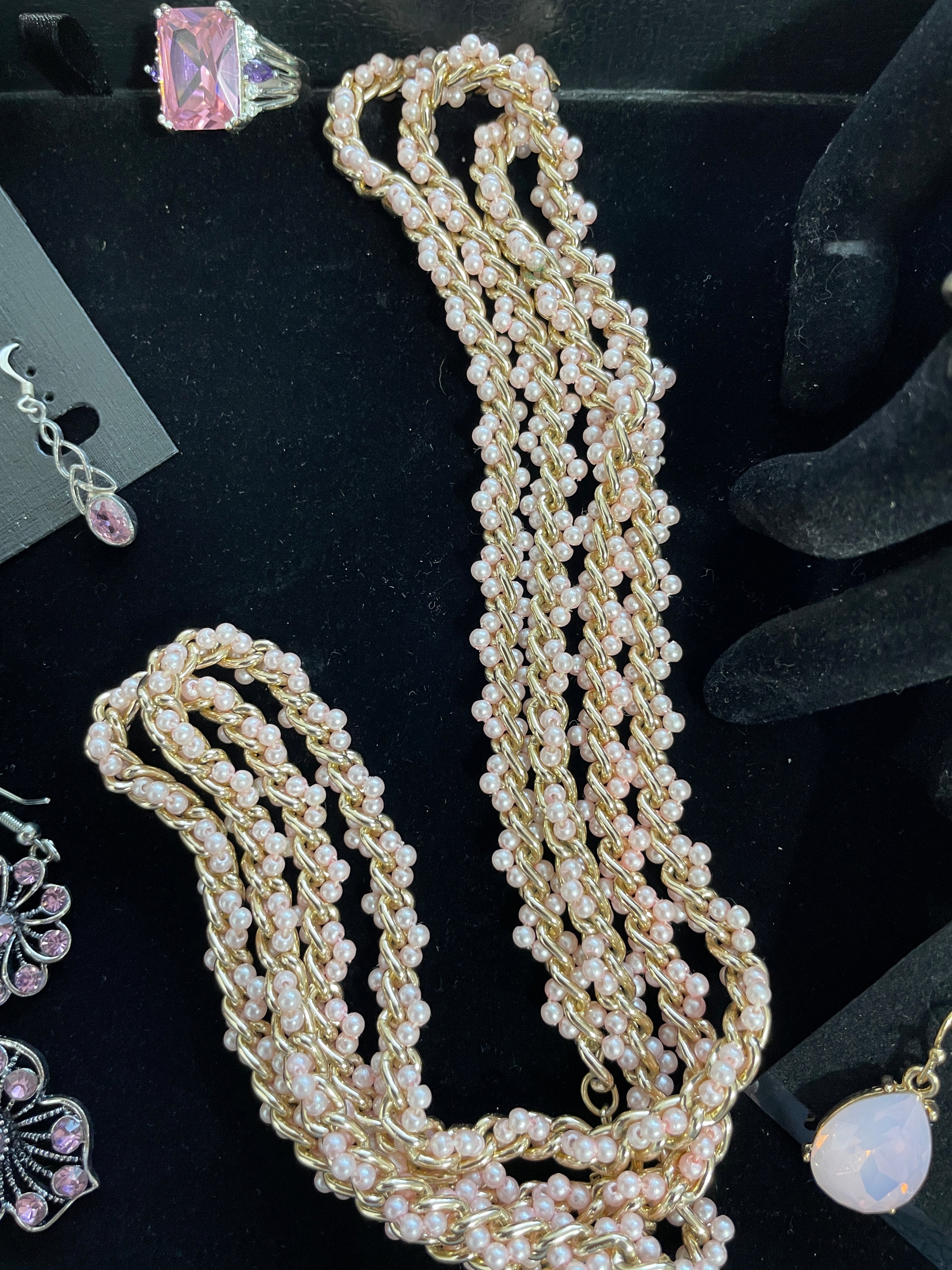 Pink beaded necklace on a black background with other jewelry items.