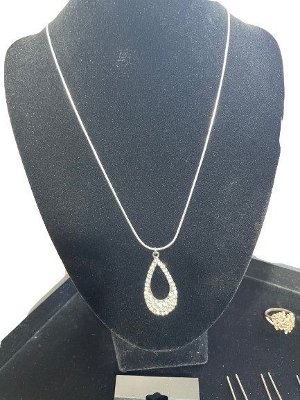 Silver teardrop pendant necklace on a black velvet stand with a ring in the background.