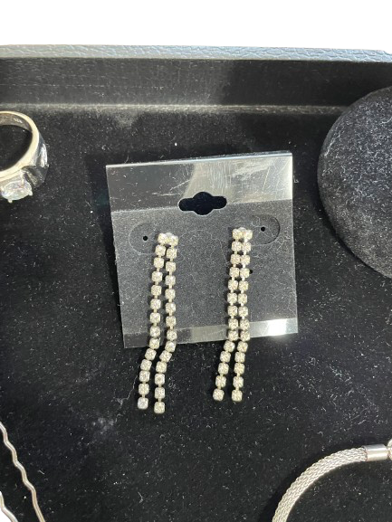 Pair of earrings on a clear card with a ring and other jewelry items on a black surface.