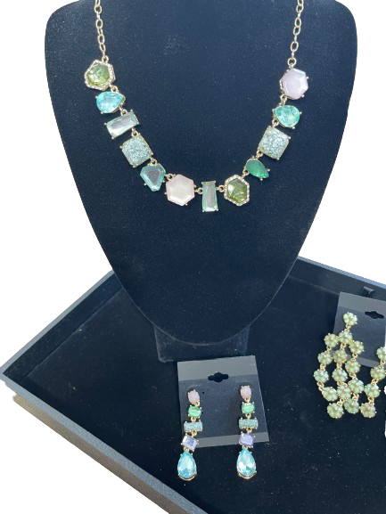 Necklace and earrings with green gemstones on a black display stand.