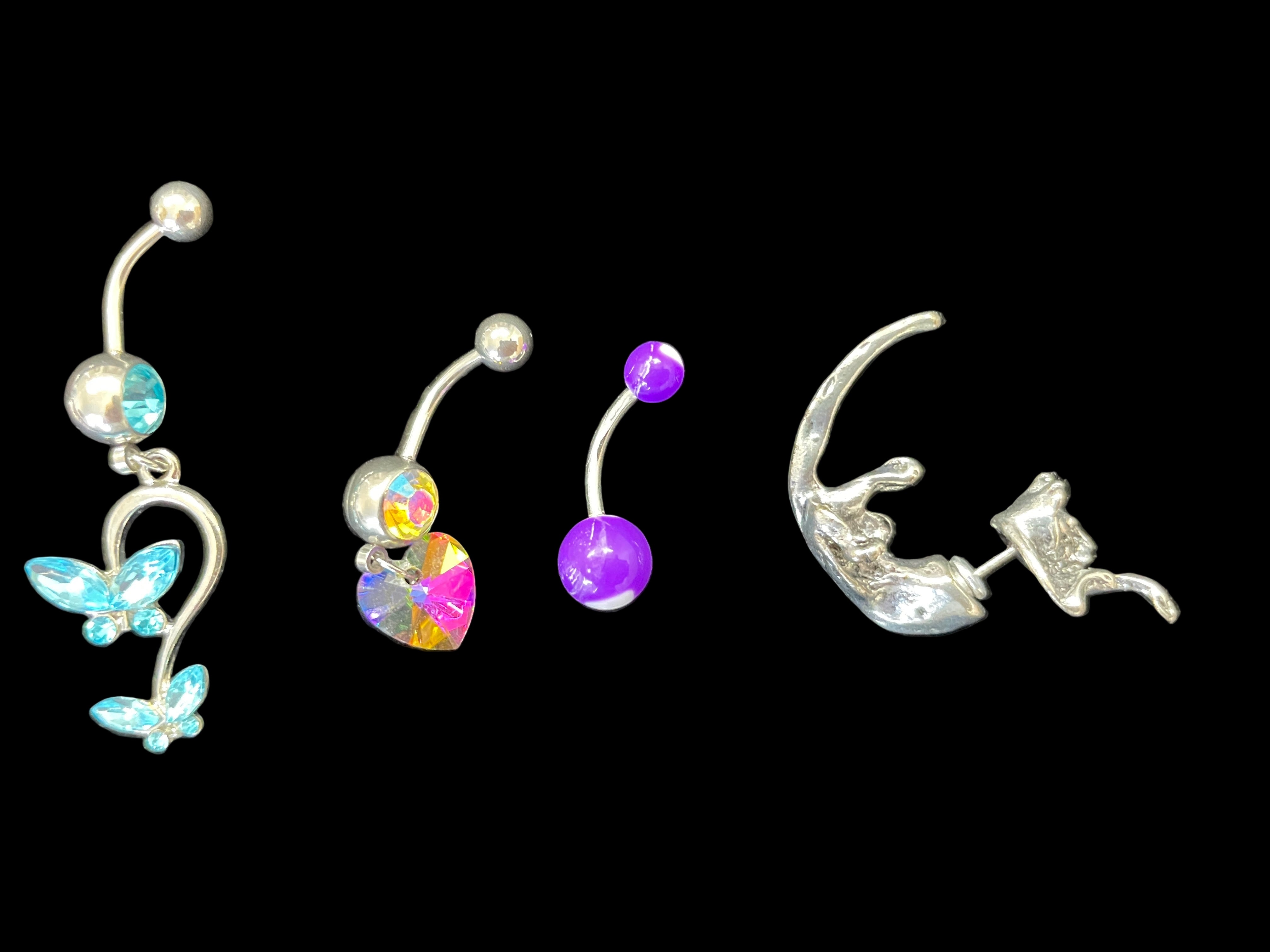 Four belly button rings with colorful gemstones on a black background
