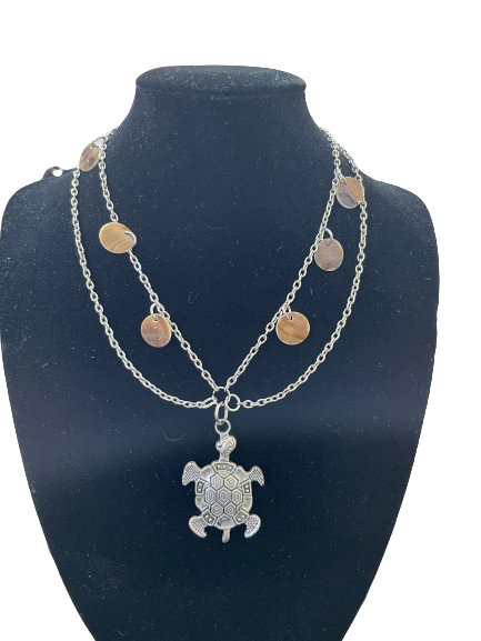 Silver-tone double-layer turtle pendant necklace with shell accents displayed on black stand