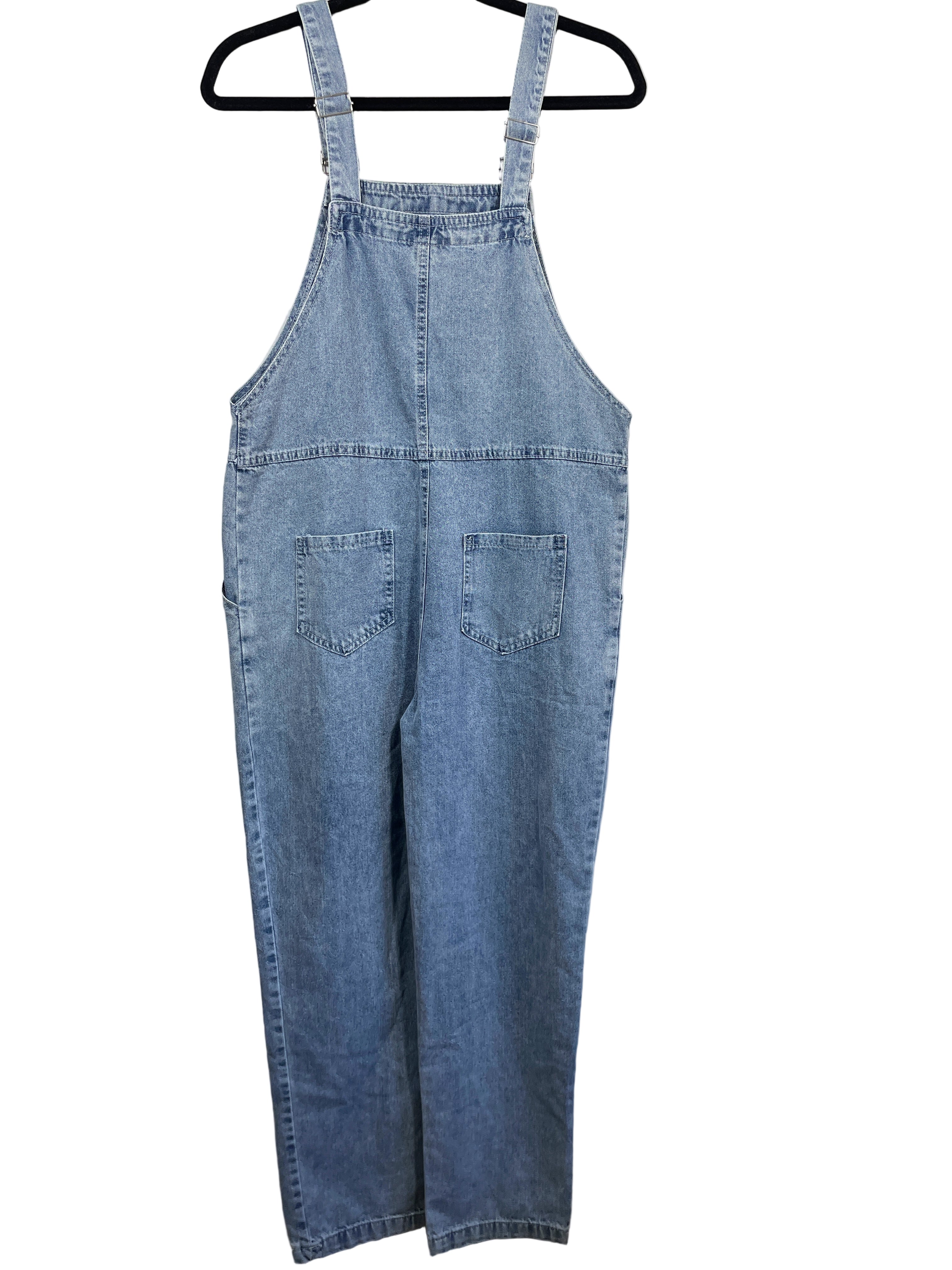 Blue denim overalls hanging on a black hanger against a white wall.