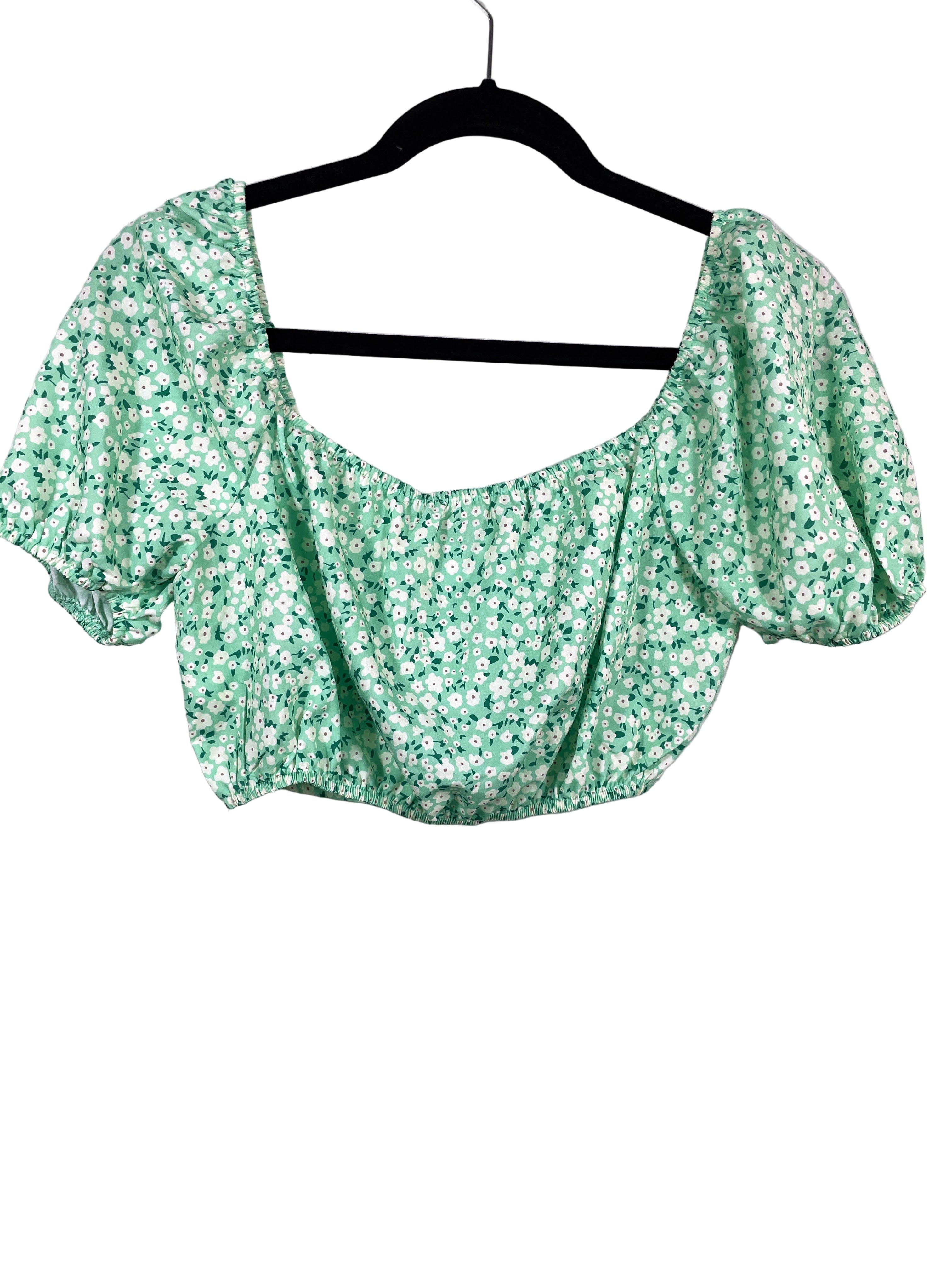 Green floral blouse on a hanger against a white background