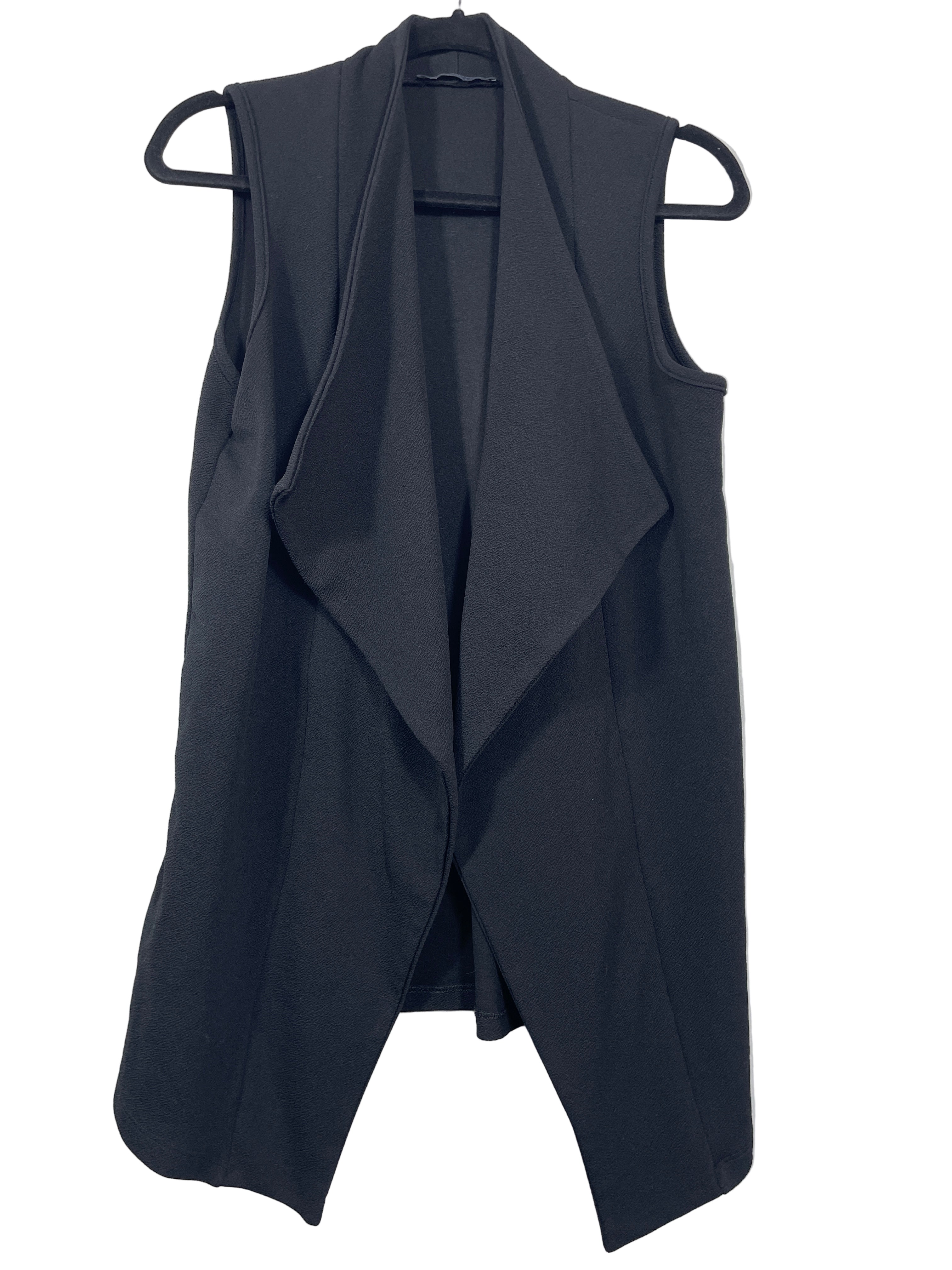 Front view of a black Suzy Shier sleeveless open-front vest hanging on a black hanger against a white wall.
